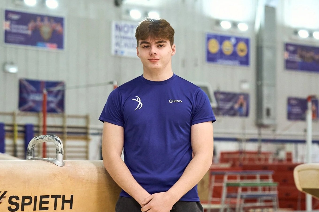 Portrait of a young man with red hair, wearing a blue shirt, facing the camera against a plain background.