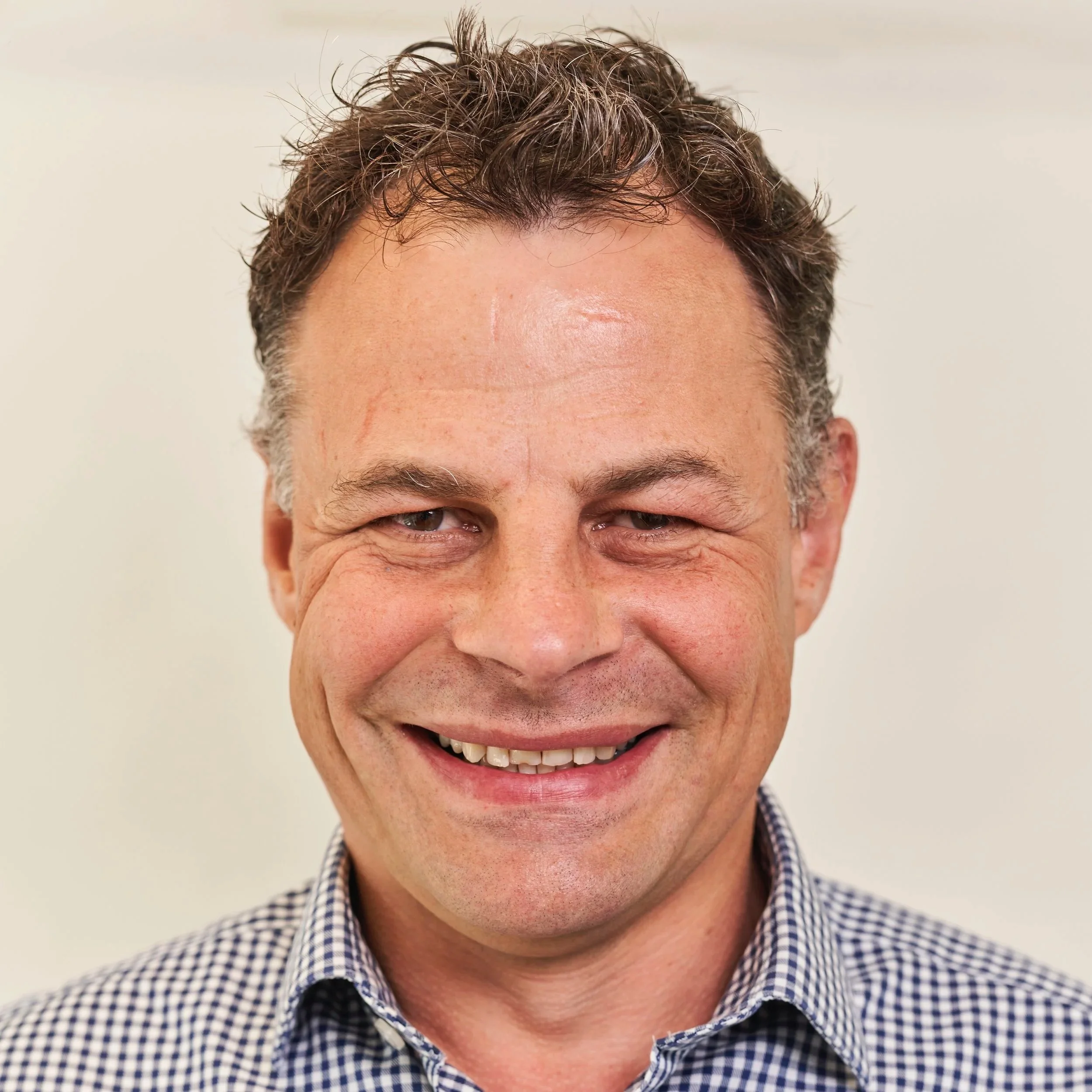 A smiling middle-aged man with curly brown hair and a checked shirt.