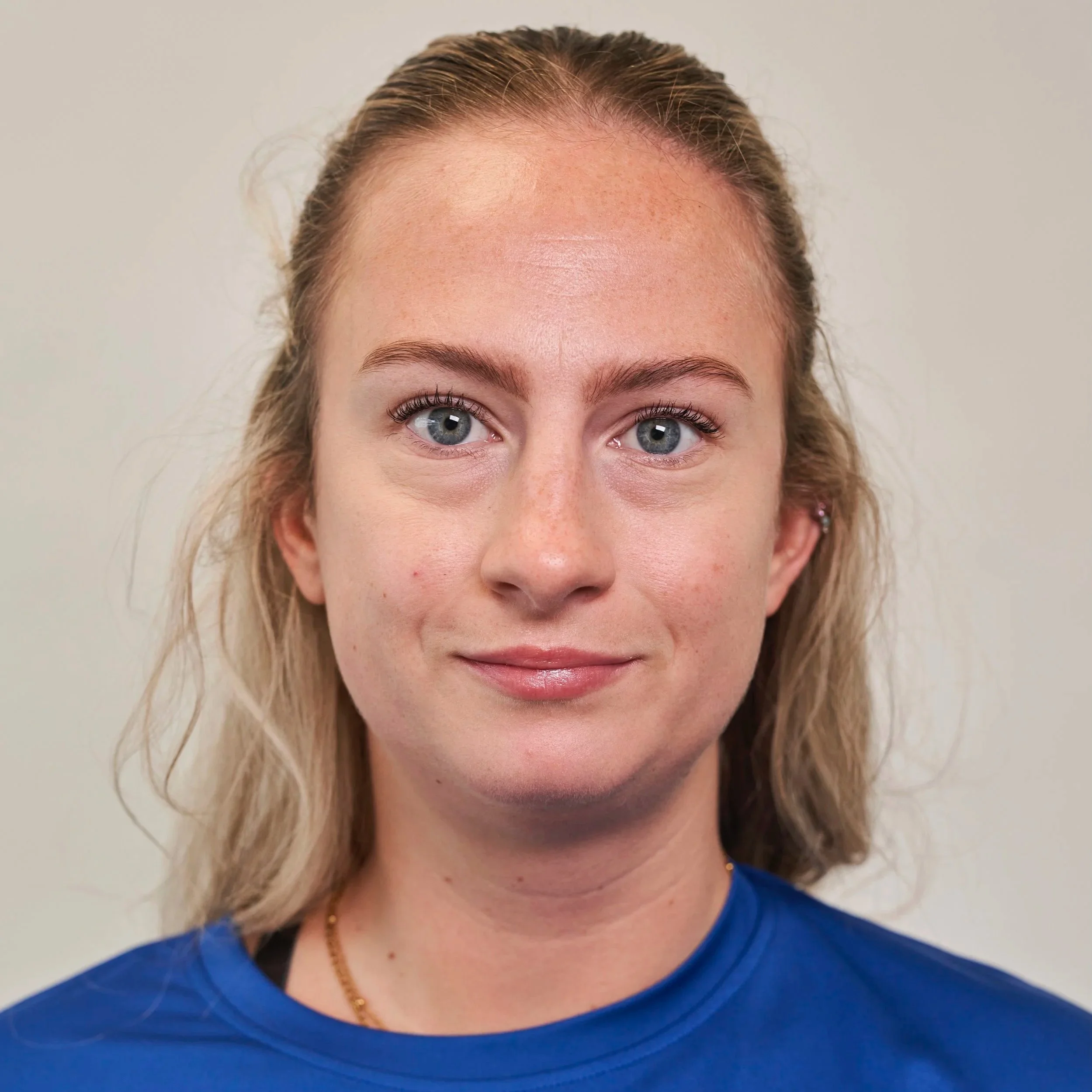 A young woman with blonde hair, blue eyes, and light skin, smiling slightly, wearing a blue shirt against a plain background.