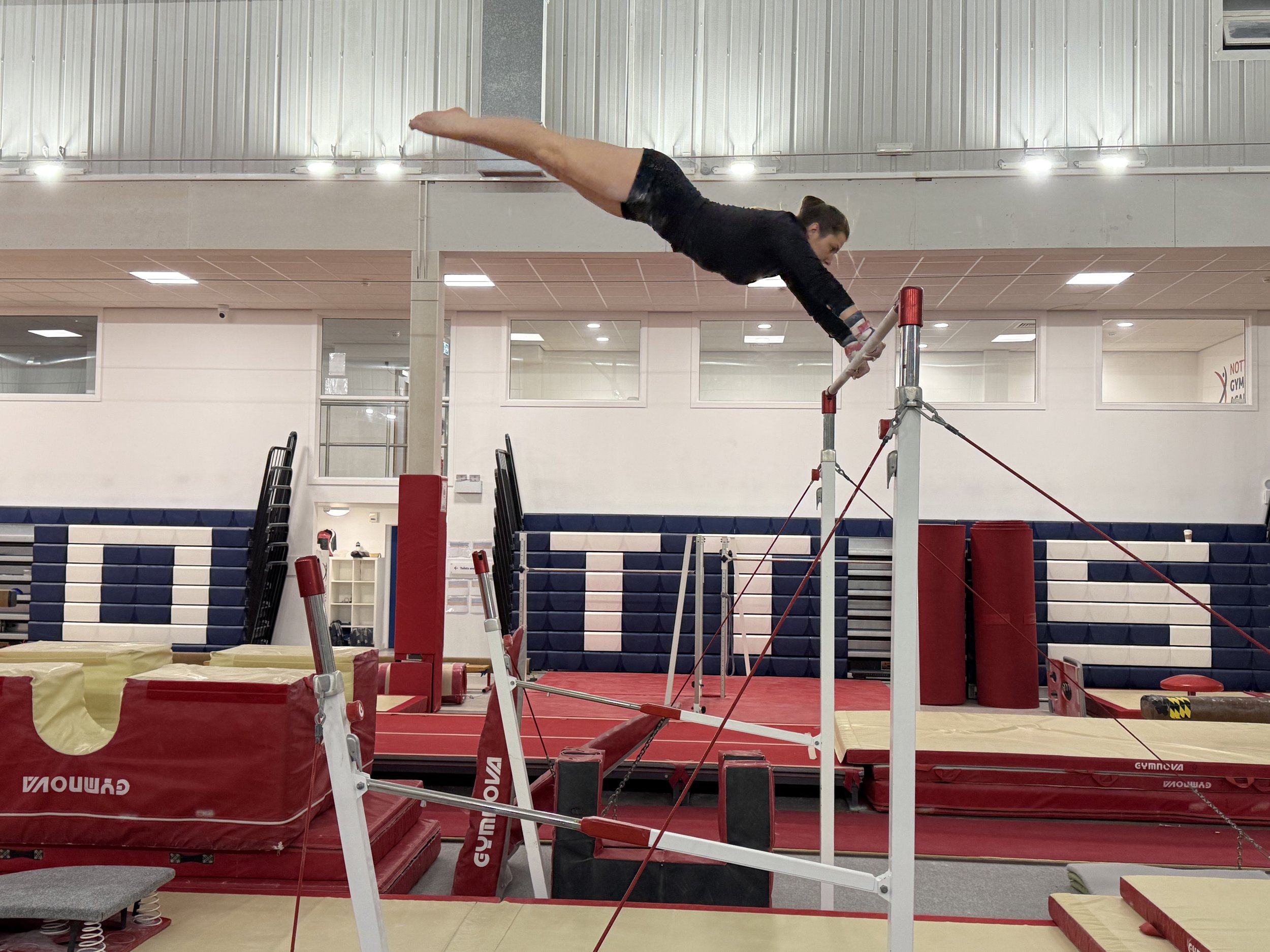 A female gymnast practicing on the uneven bars in a gymnasium.