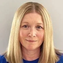 Close-up of a woman with long blonde hair, fair skin, and wearing a blue top, smiling softly at the camera.