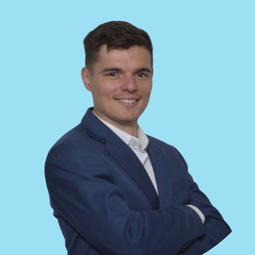 A man with short brown hair, wearing a blue suit, smiling against a light blue background.