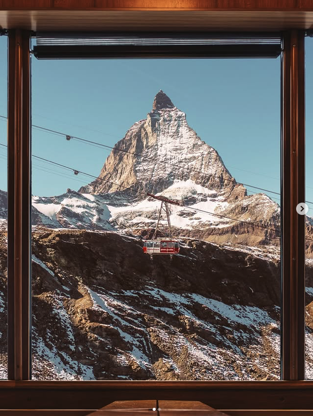 View of snow-capped mountain, likely the Matterhorn, through a window with a cable car in the foreground.