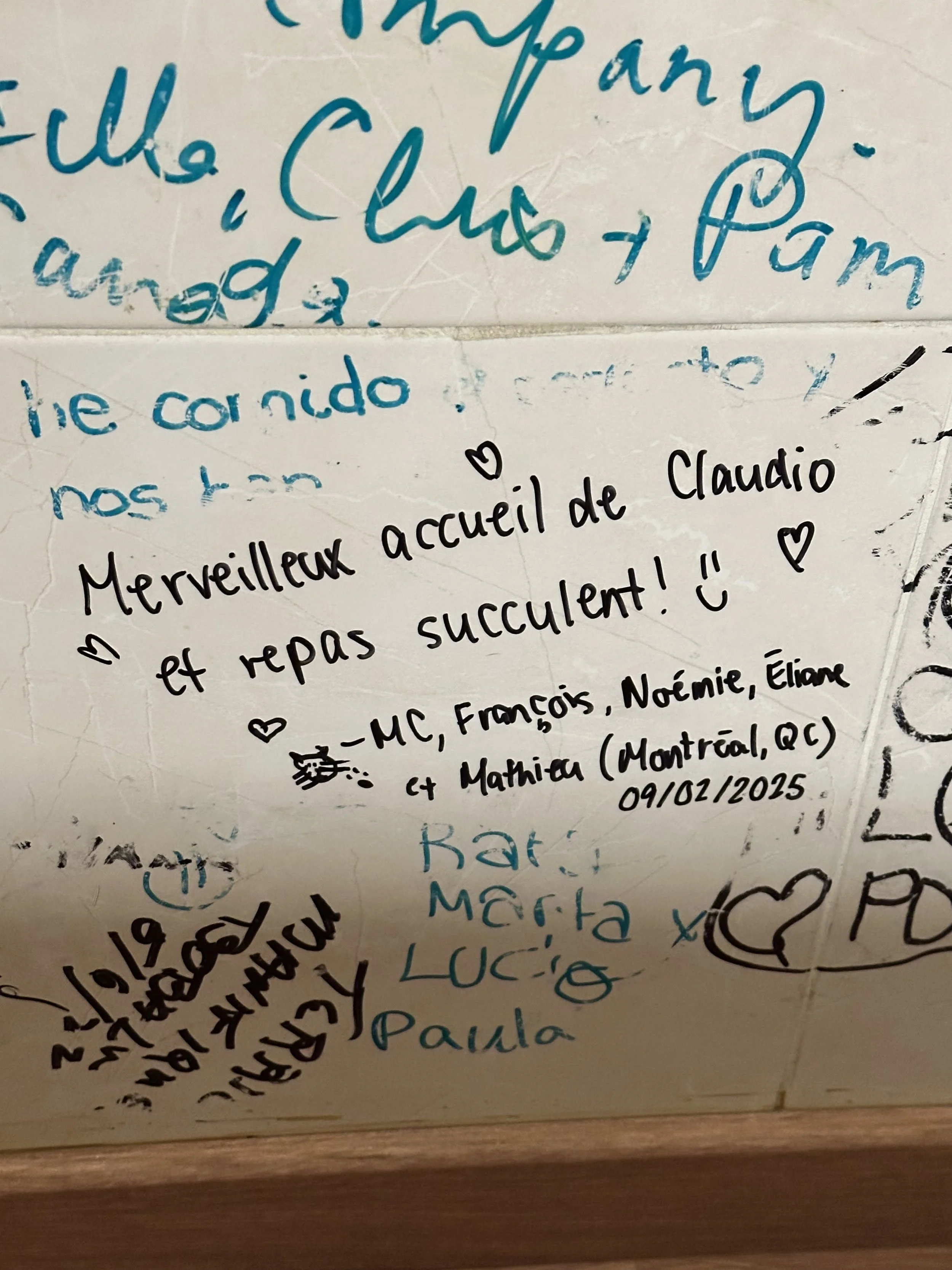A wall with handwritten notes and messages in French and Spanish, with some drawings and doodles.