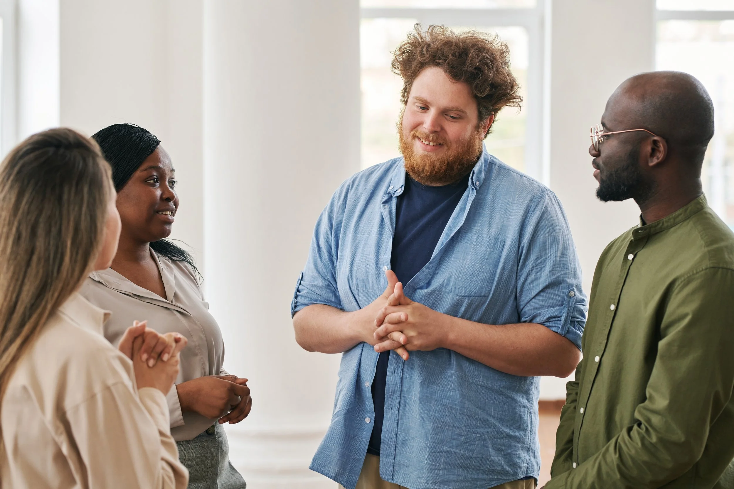 A diverse group of five people engaged in a friendly conversation indoors, smiling and listening.