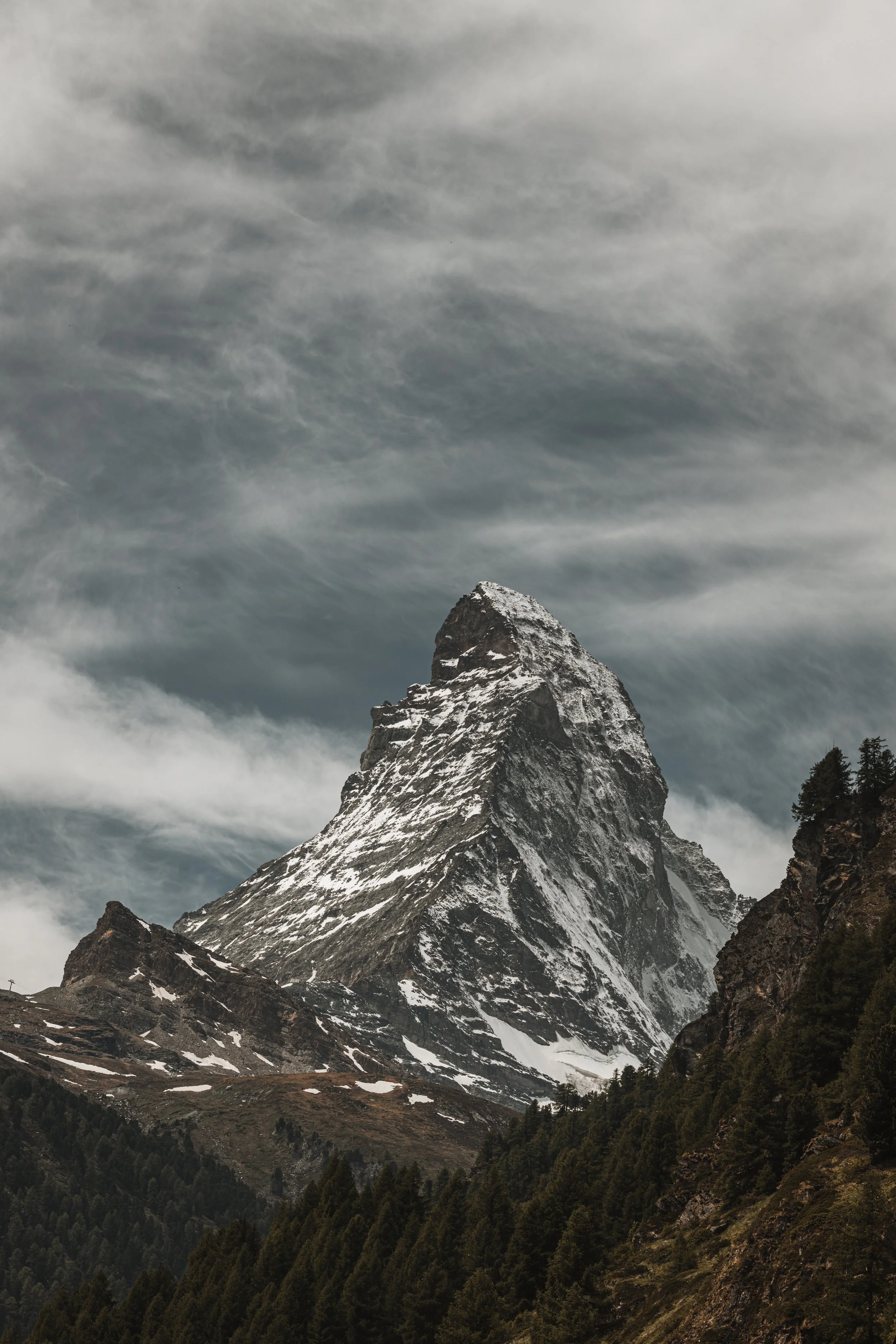 Snow-capped mountain peak with cloudy sky and forested slopes.