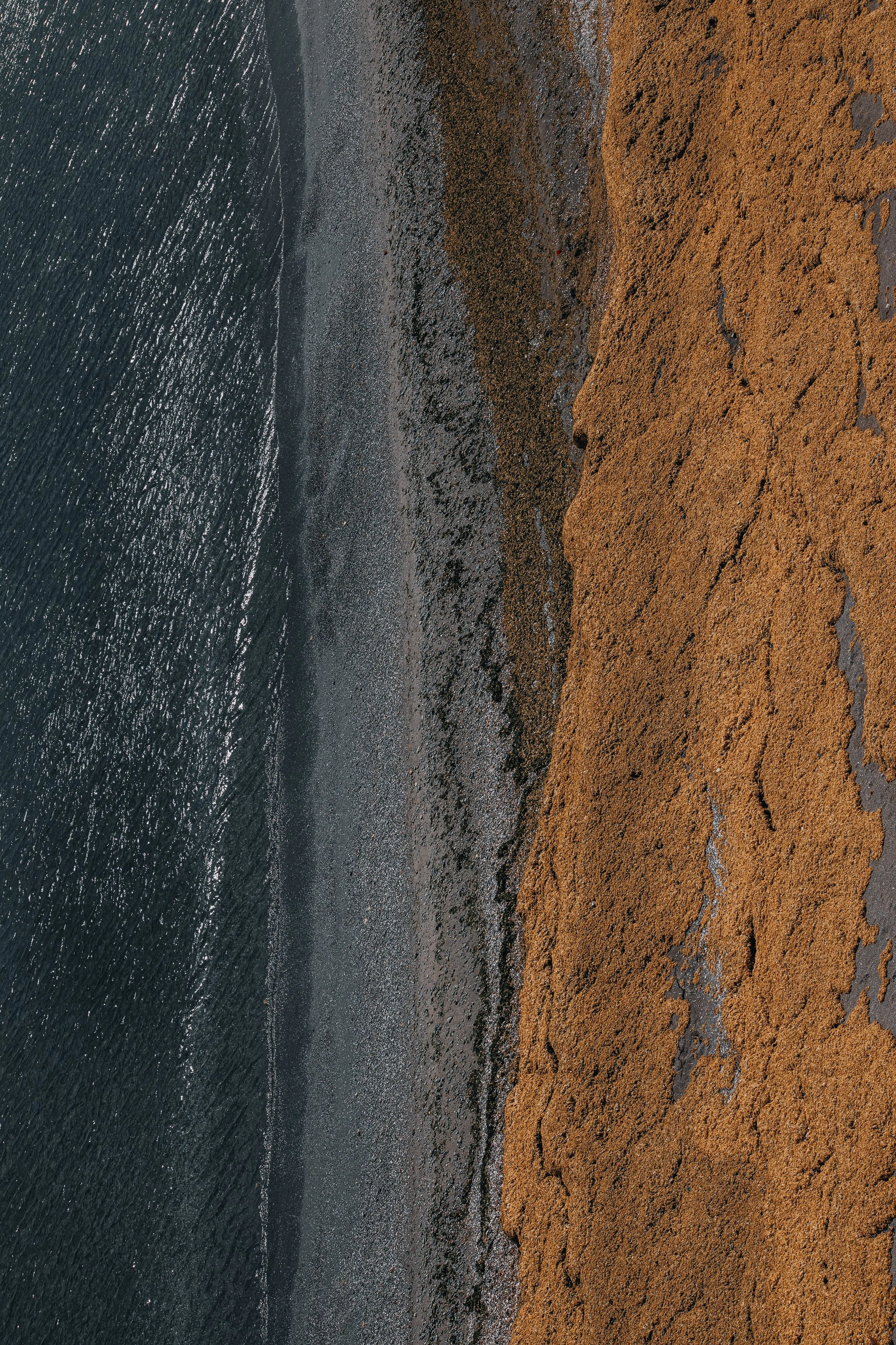 Aerial view of a rocky beach with ocean waves on the left and orange-brown cliff on the right.