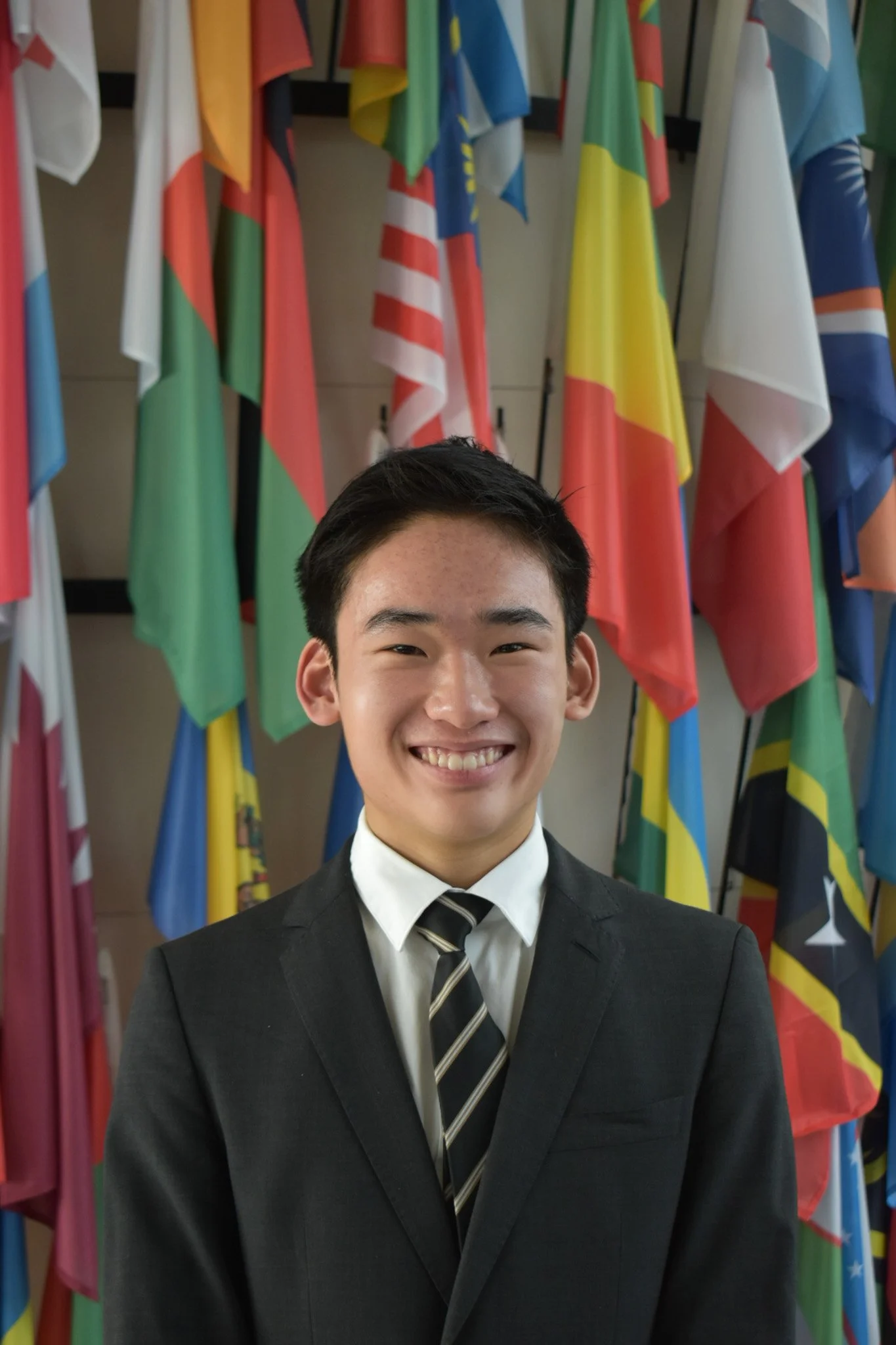 Young man smiling, wearing a pink shirt, with short black hair, against a gray background.
