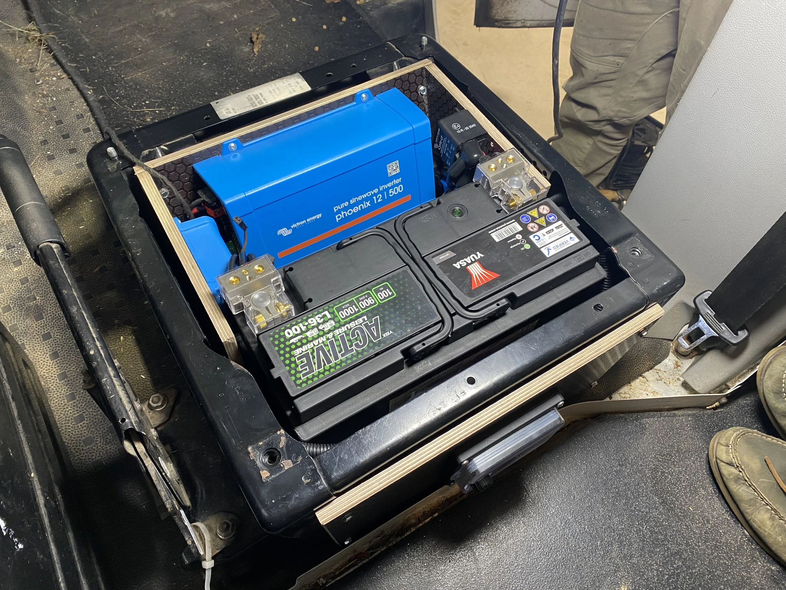 Inside view of a battery pack enclosure showing a blue pure sine wave inverter, two black batteries with labels, and some wiring.