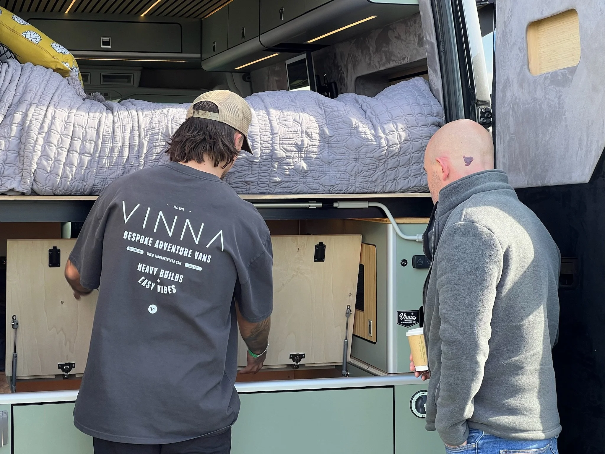 Two men inspecting inside a VW Crafter camper van with a raised bed.