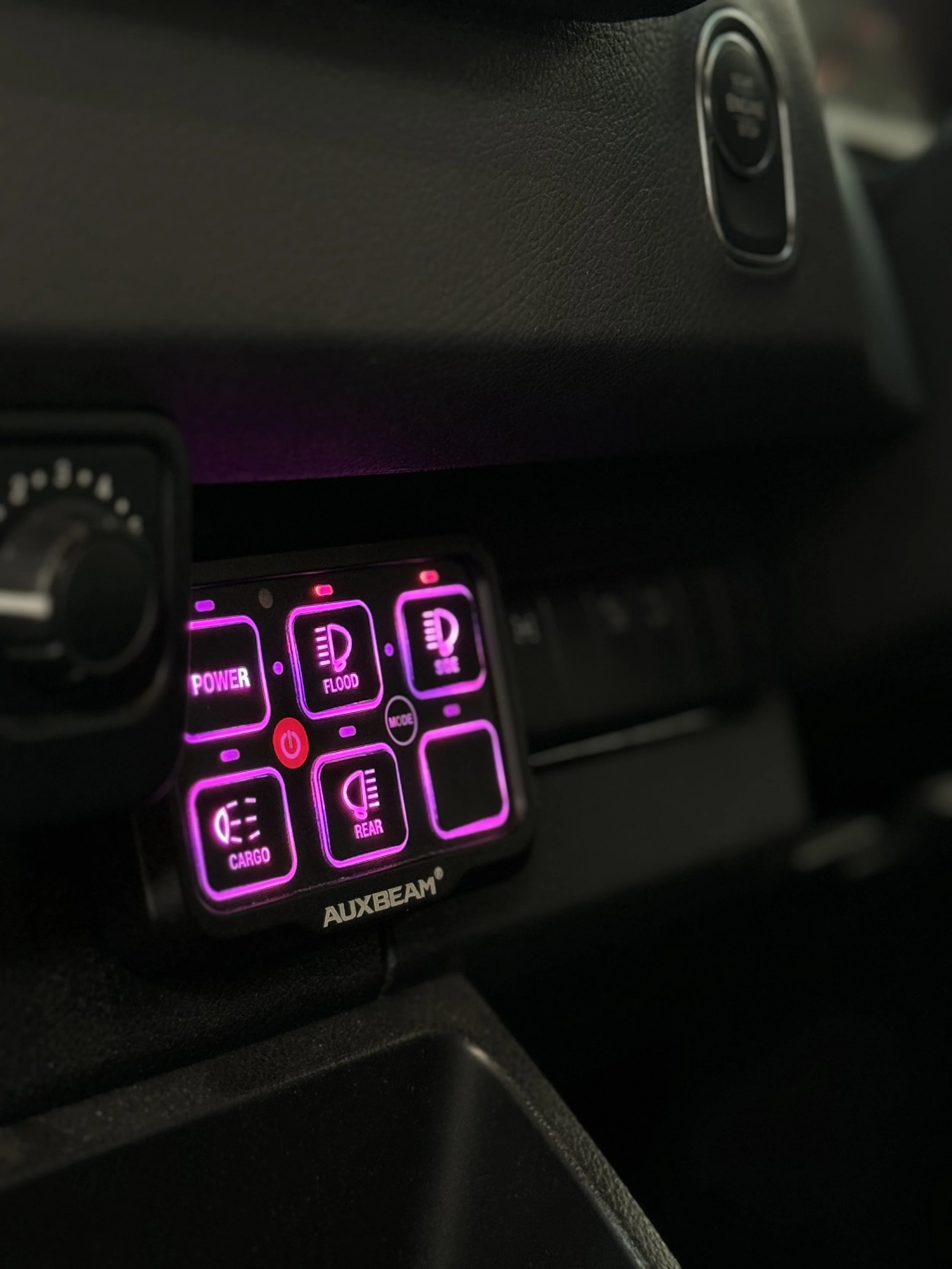 Illuminated AUXBEAM control panel in a vehicle with labeled buttons for power, flood, high beams, cargo, rear, and a mode button, all with pink backlighting.