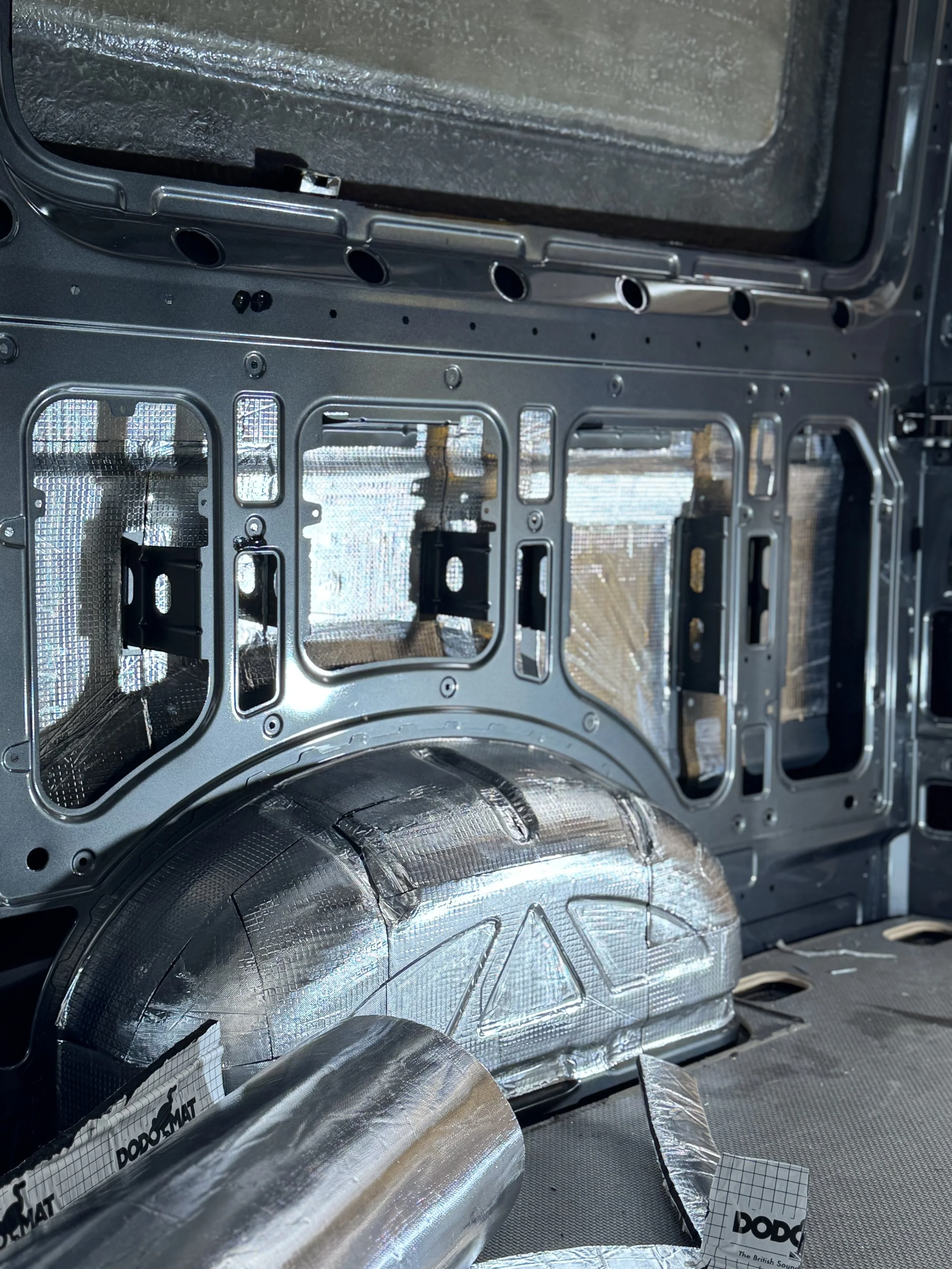 The interior of a vehicle showing exposed metal framework and insulation, with some fiberglass insulation and foil heat shielding.