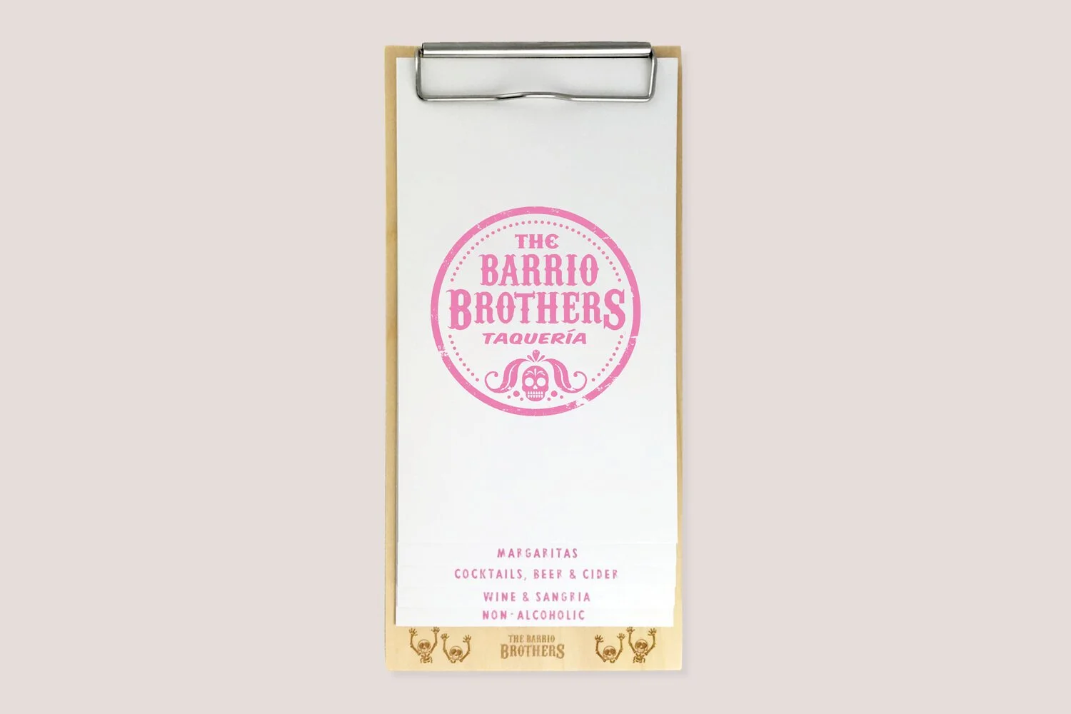 Menu with pink circular logo for The Barrio Brothers Taqueria on white paper clip on beige background, listing food and drink options.
