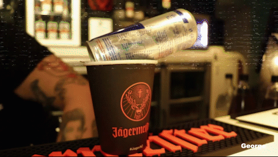 A can of Red Bull energy drink balanced on top of a black Jägermeister shot glass on a bar counter.