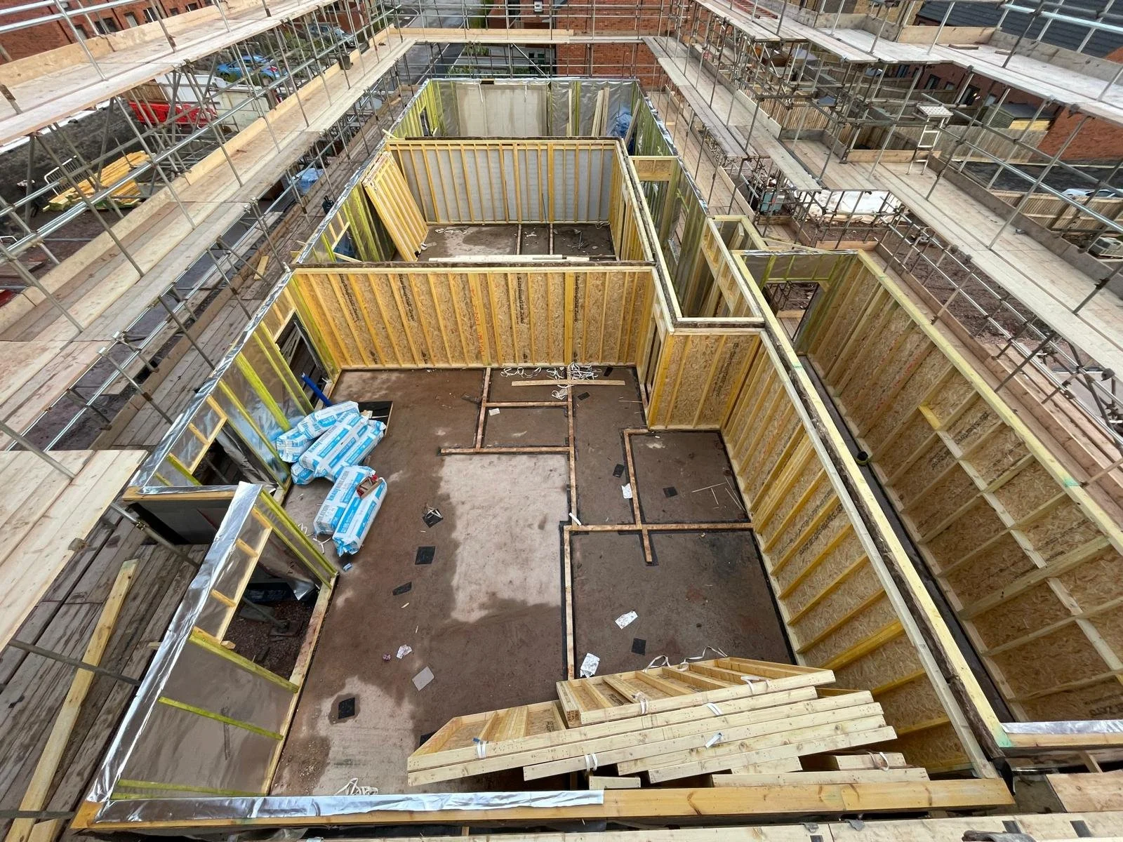 Construction site with wooden framing and scaffolding for a building, showing an interior layout with insulation materials and exposed wiring.
