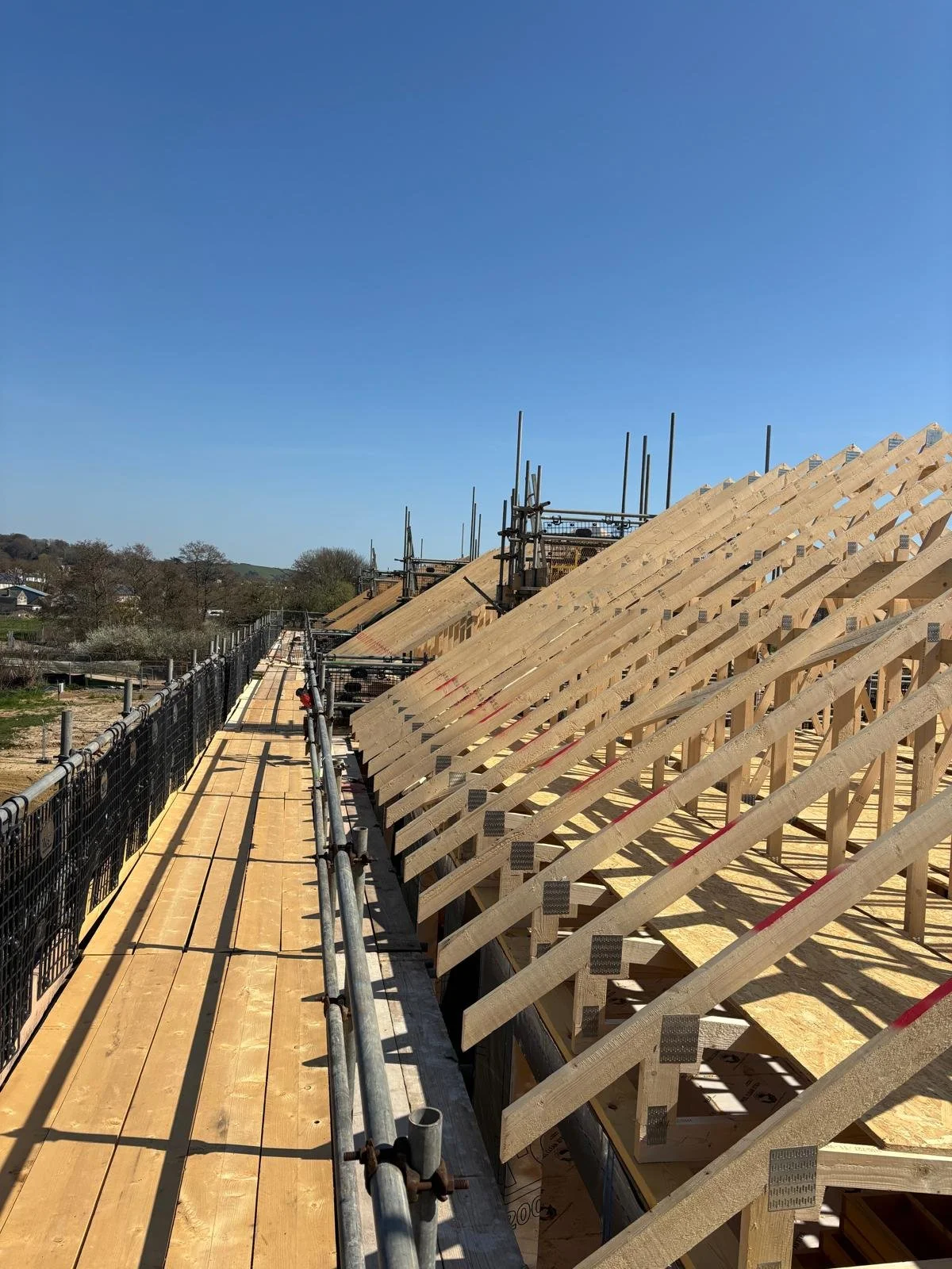 Construction site with wooden roof trusses being assembled on a building under clear blue sky.
