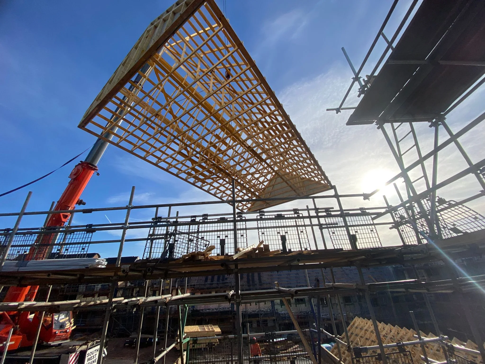 Construction site with scaffolding and a wooden framework being assembled under a blue sky with the sun shining.