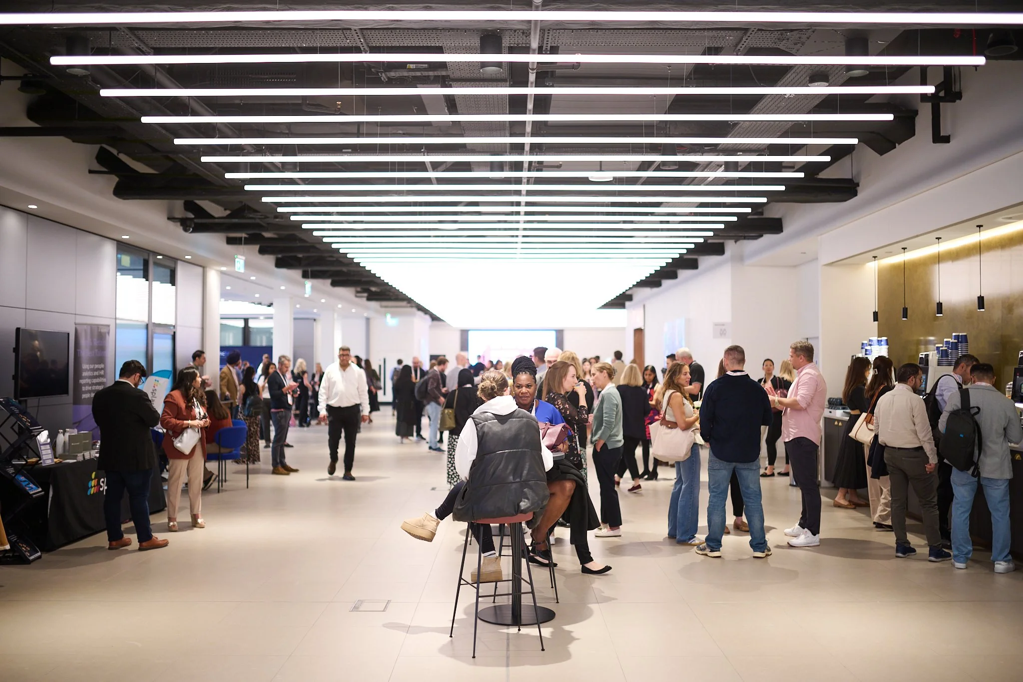 People networking in a modern conference hall with seating and refreshments.