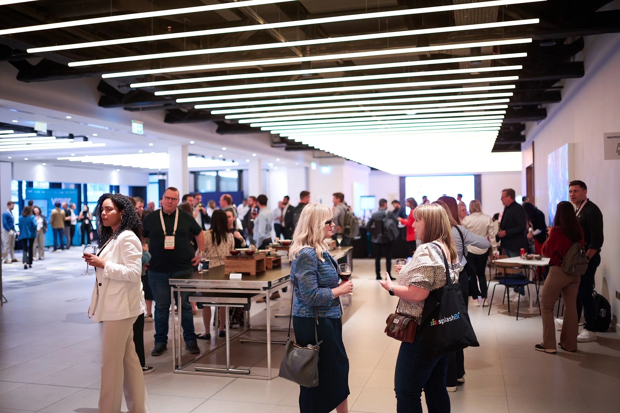 People networking at a business event in a modern indoor setting, with groups engaged in conversation.