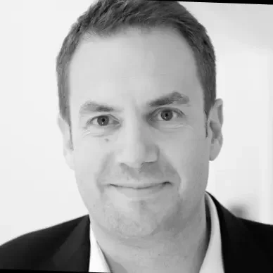 A black-and-white headshot of a man with short hair, wearing a suit jacket and shirt, smiling at the camera.