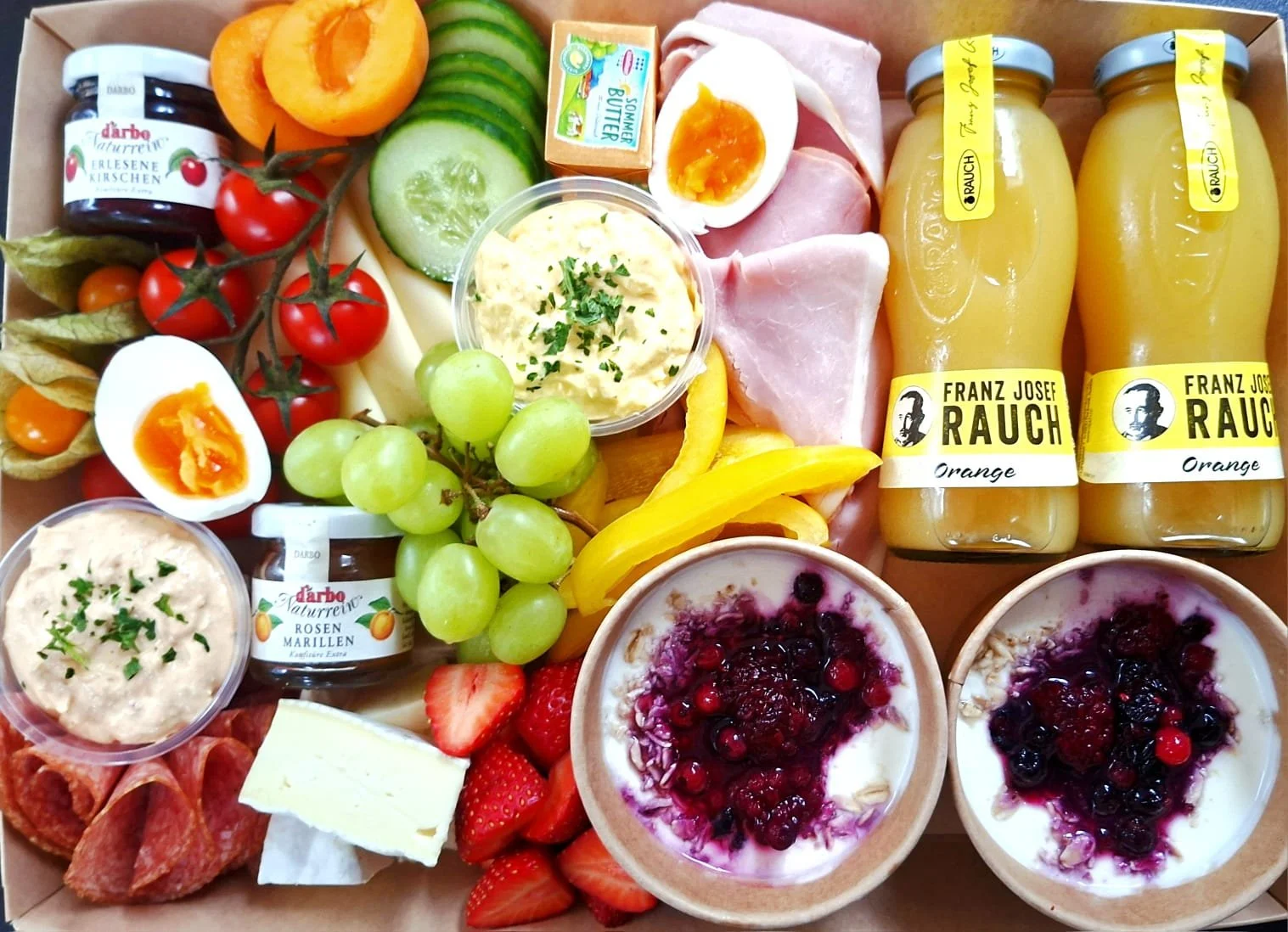 Der Inhalt einer Brunchbox wie Ost, Früchte, Getränke und Aufstriche