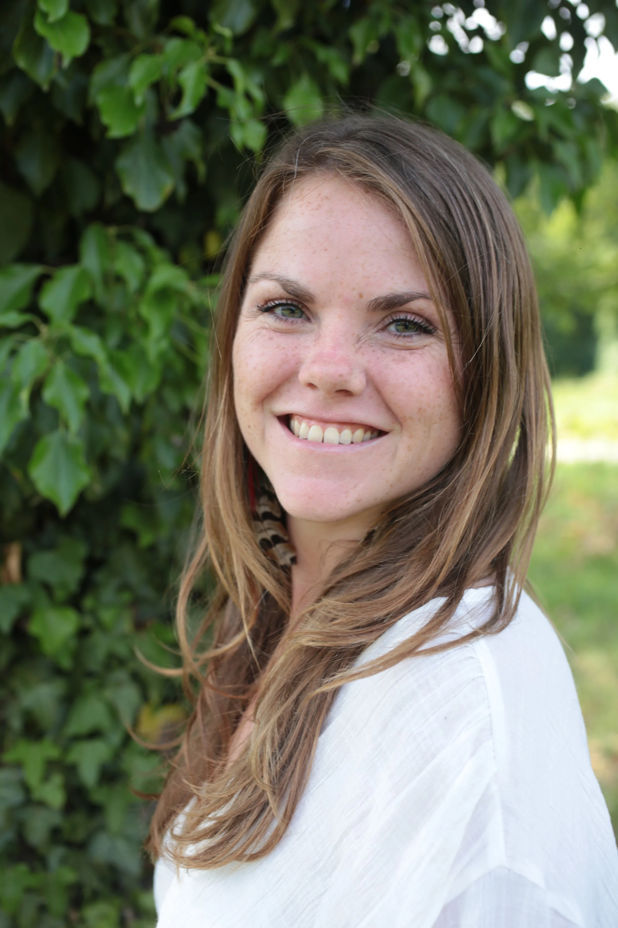 Ein lächelndes junges Mädchen mit braunen Haaren vor Grünflächen.