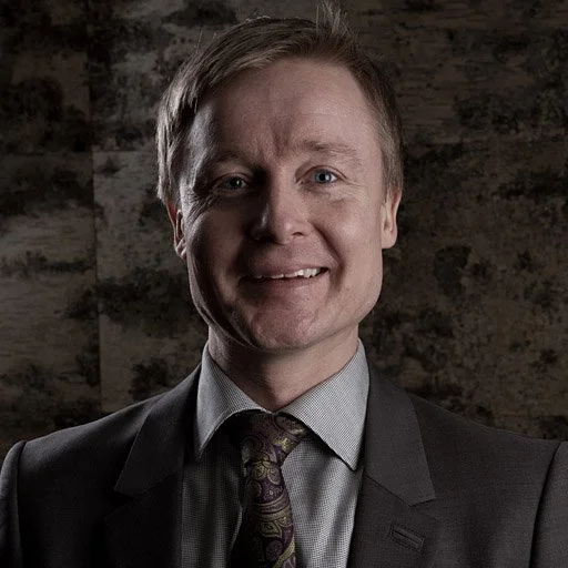 Mies puki tummanharmaassa pukupuvussa hymyillen kameraan.