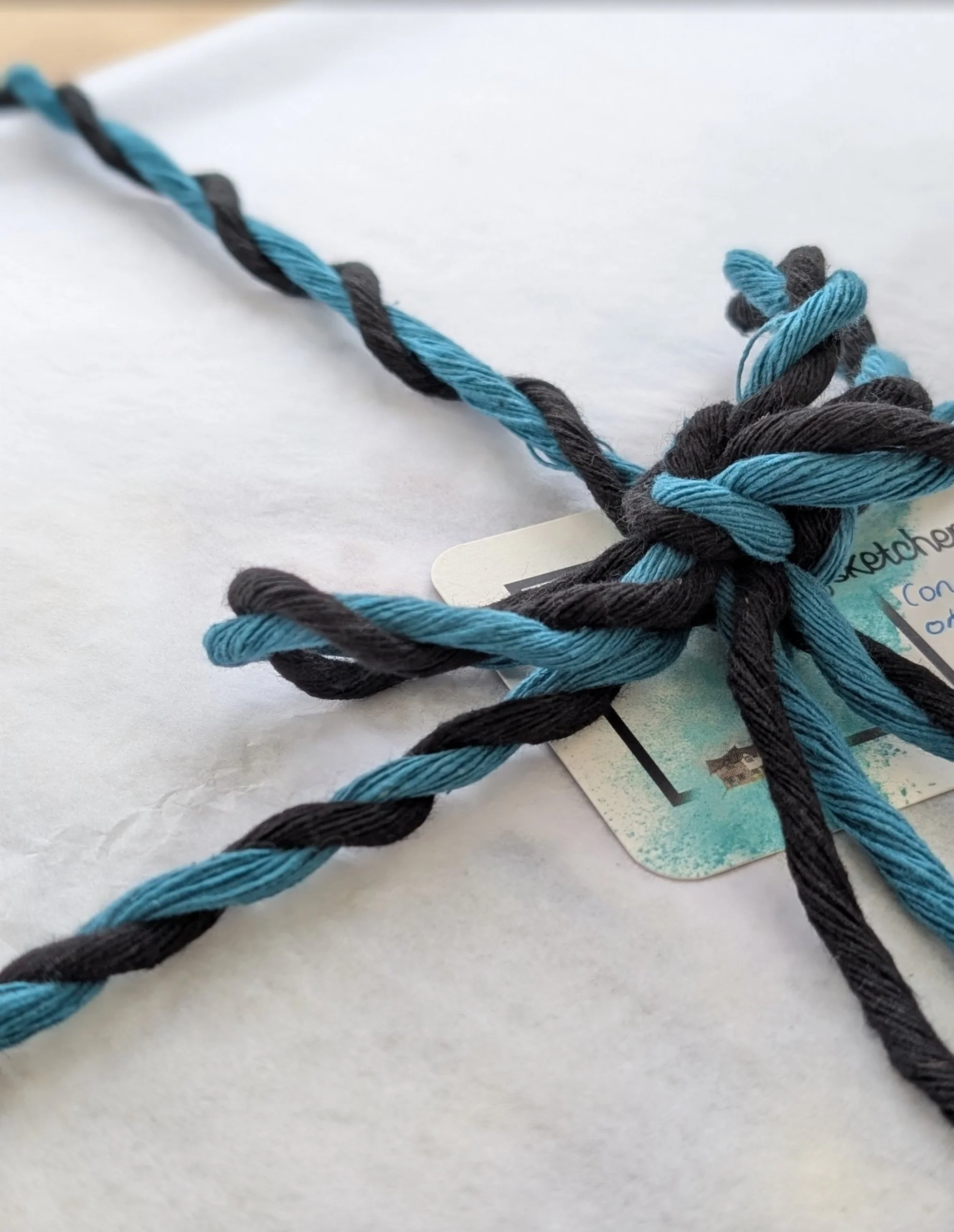 A gift wrapped portrait, wrapped in white tissue paper with twisted blue and black embroidery thread for decoration.