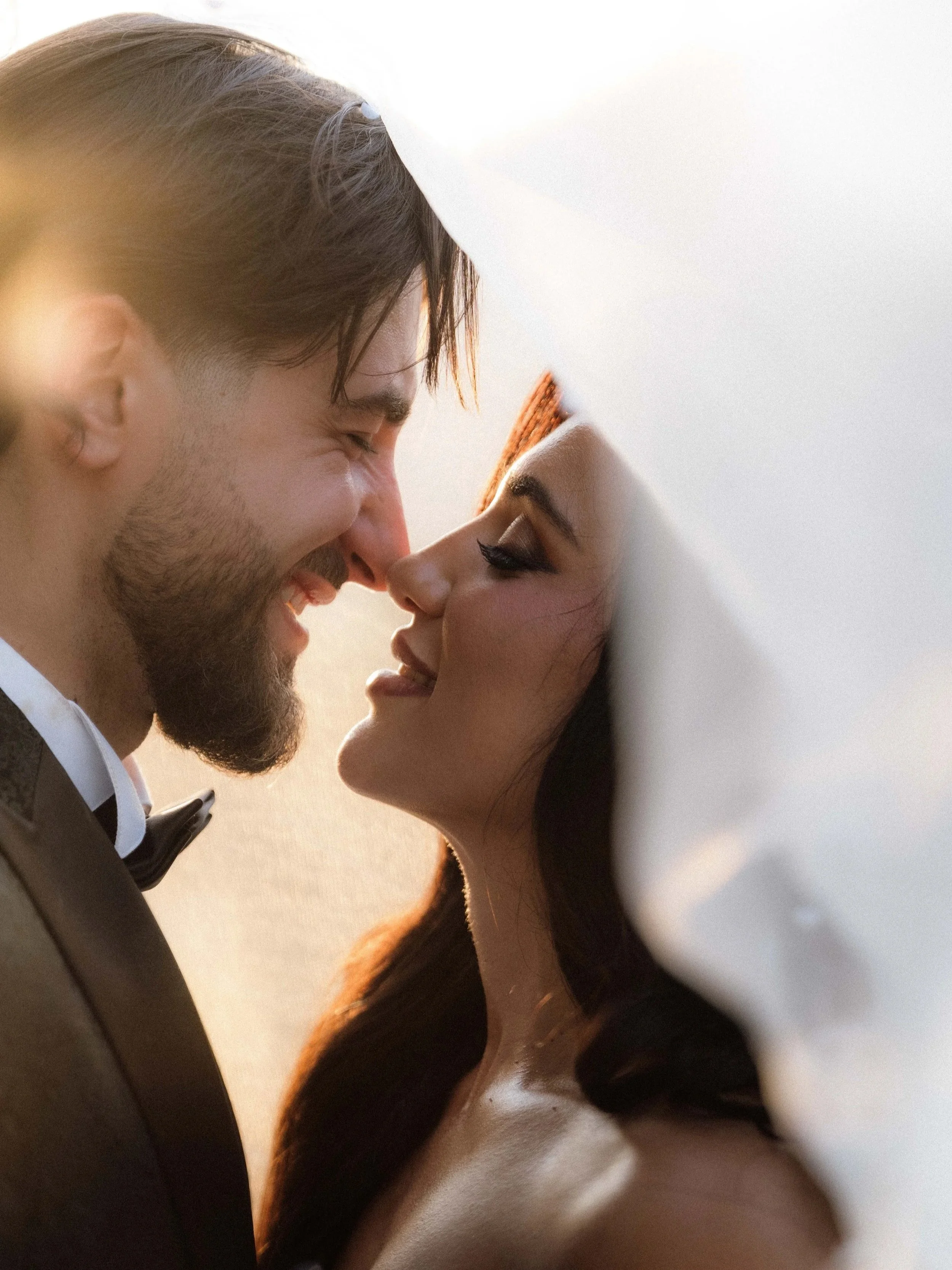 A man and woman with their foreheads and noses touching, smiling and sharing an intimate moment.