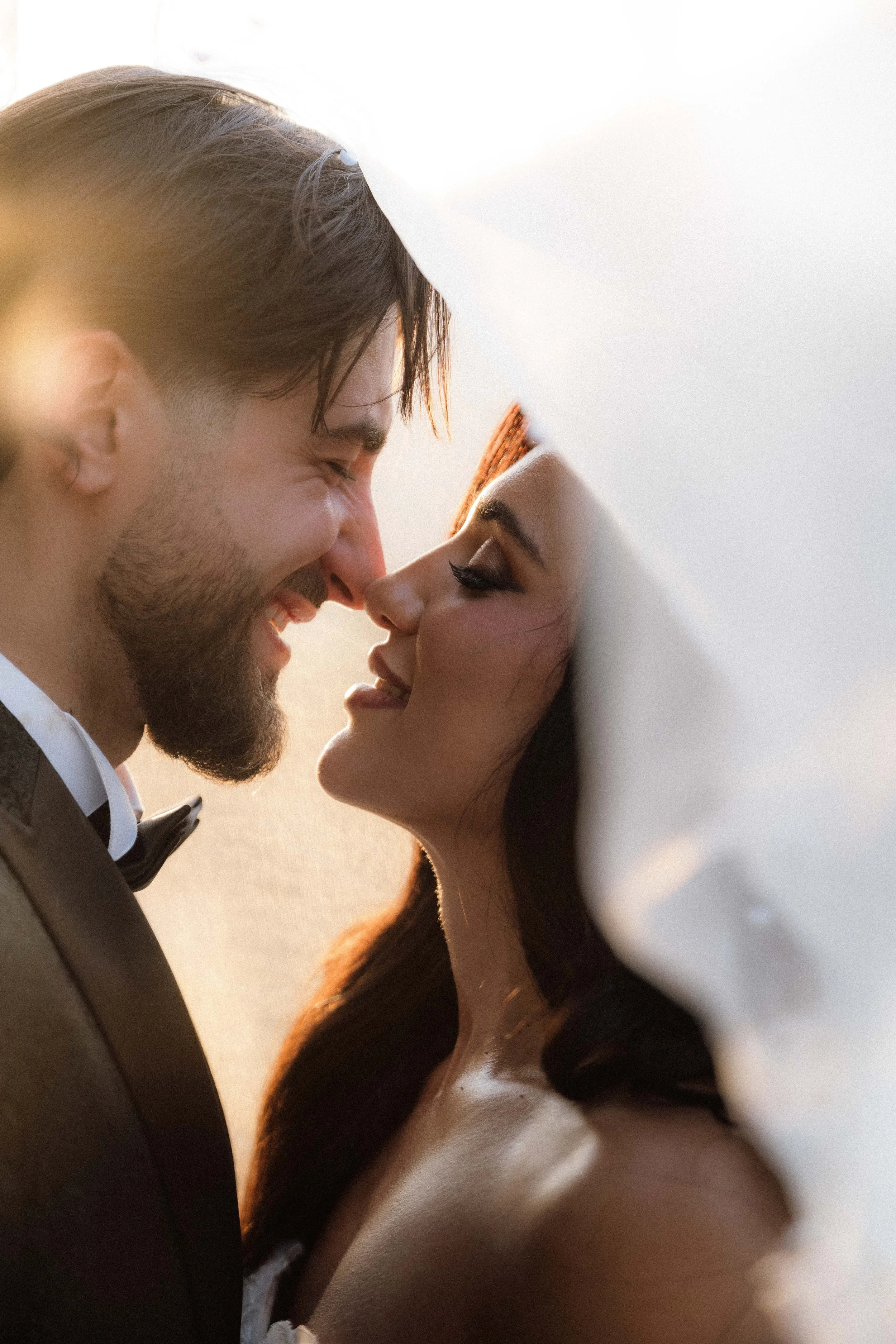 A close-up of a man and woman with foreheads touching, both smiling gently with eyes closed, in a romantic moment.