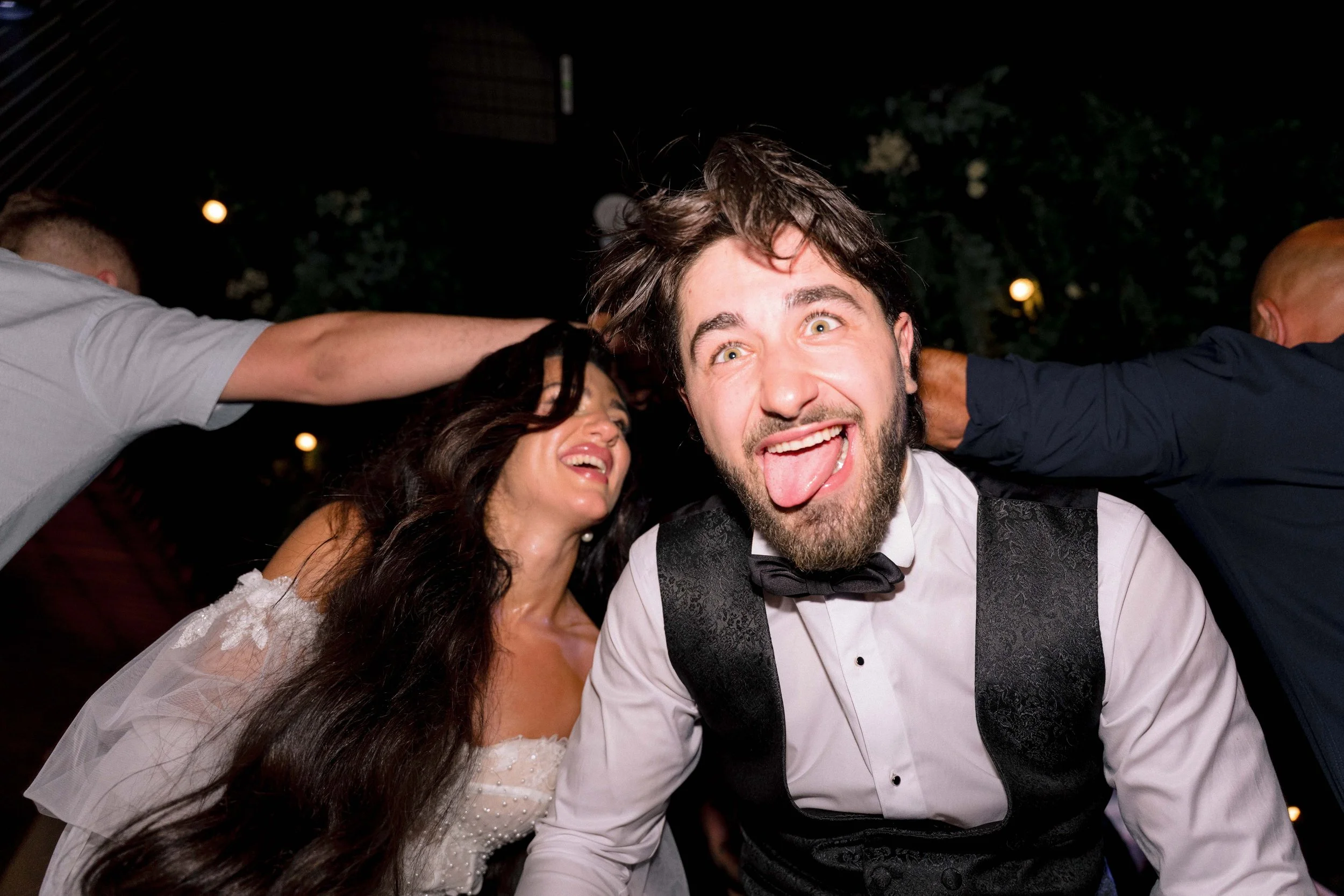 People celebrating at a party, smiling, young man sticking out his tongue, woman laughing, night setting.