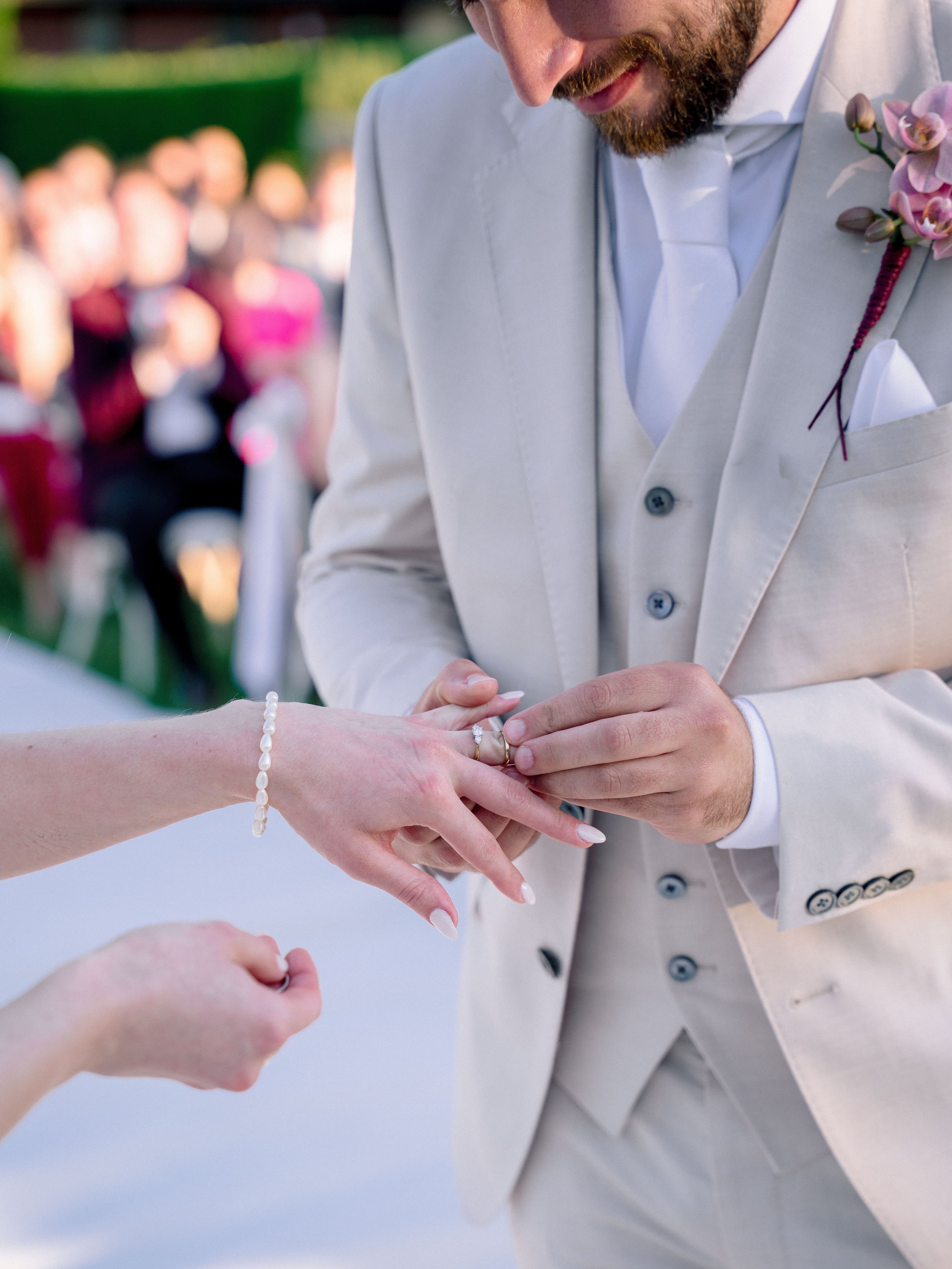 A man in a light gray suit is placing a wedding ring on a woman's finger during a wedding ceremony.