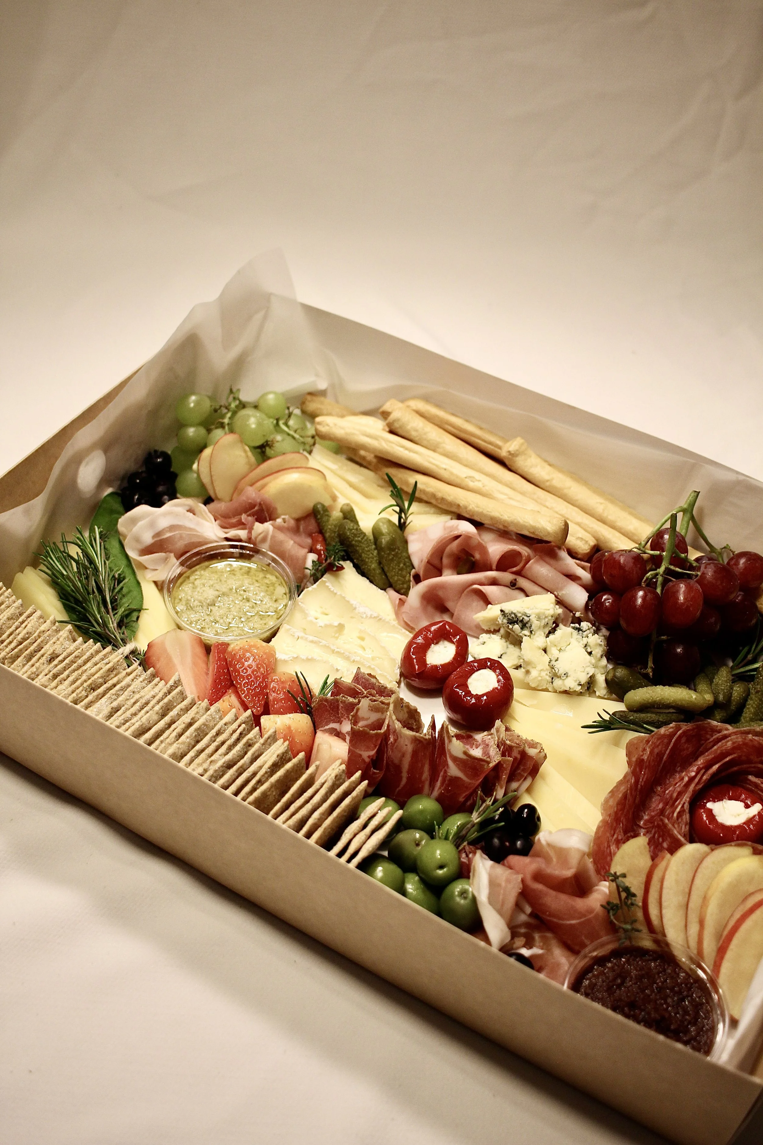 A charcuterie board with assorted cheeses, cured meats, grapes, strawberries, apple slices, crackers, and condiments.