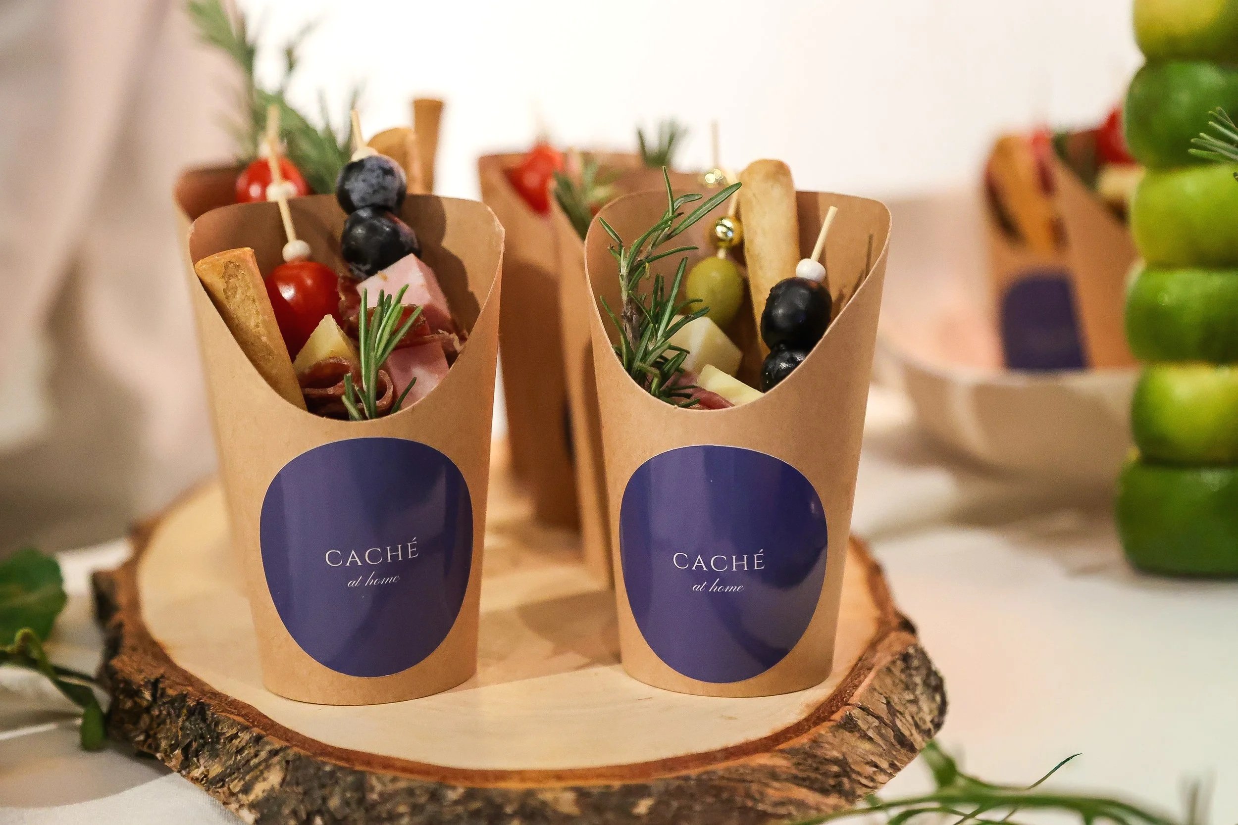 Three paper cones filled with appetizers, garnished with herbs and skewers, placed on a wooden slice on a table.