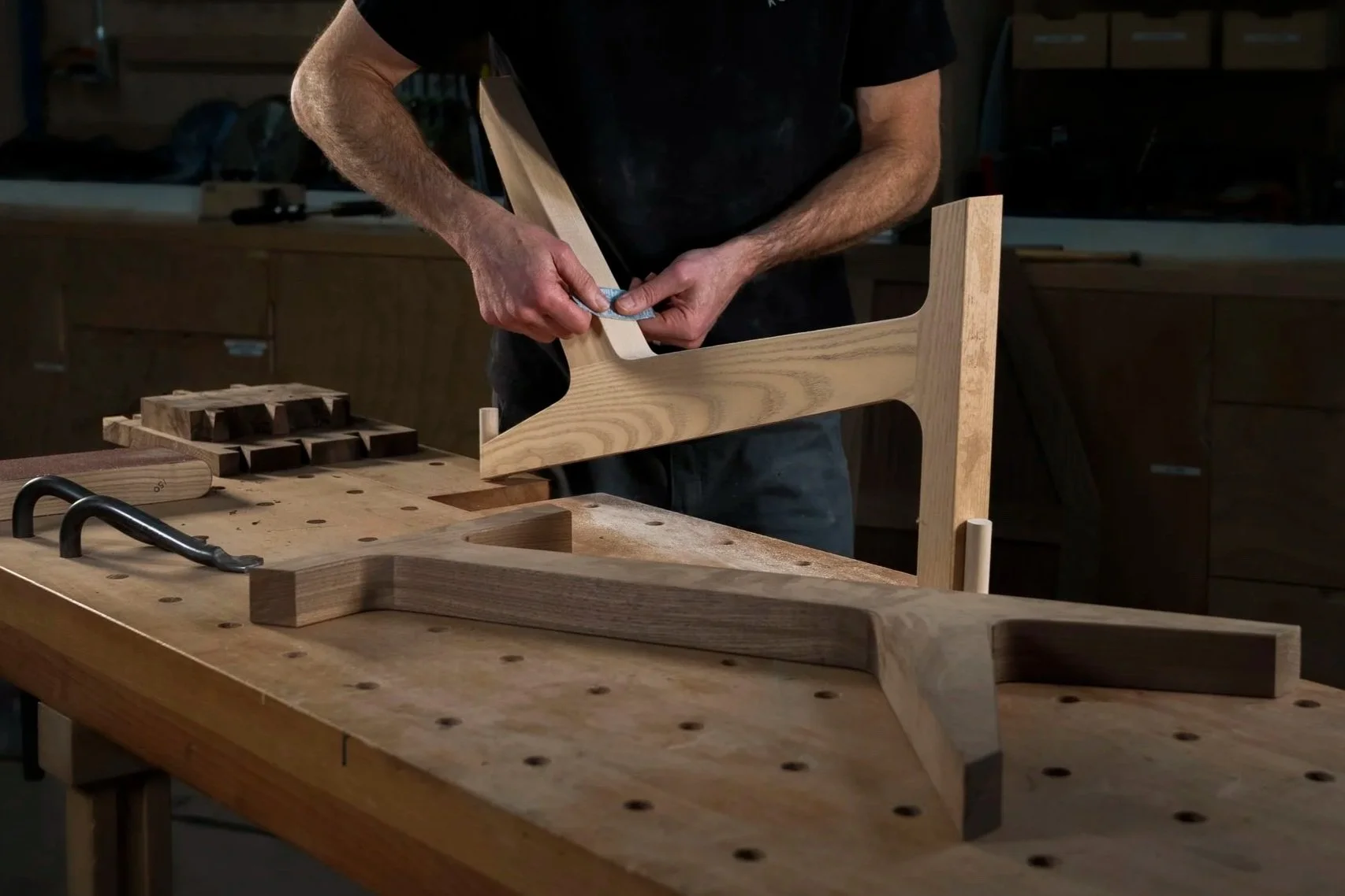 A woodworker sanding a wooden leg on a workbench.