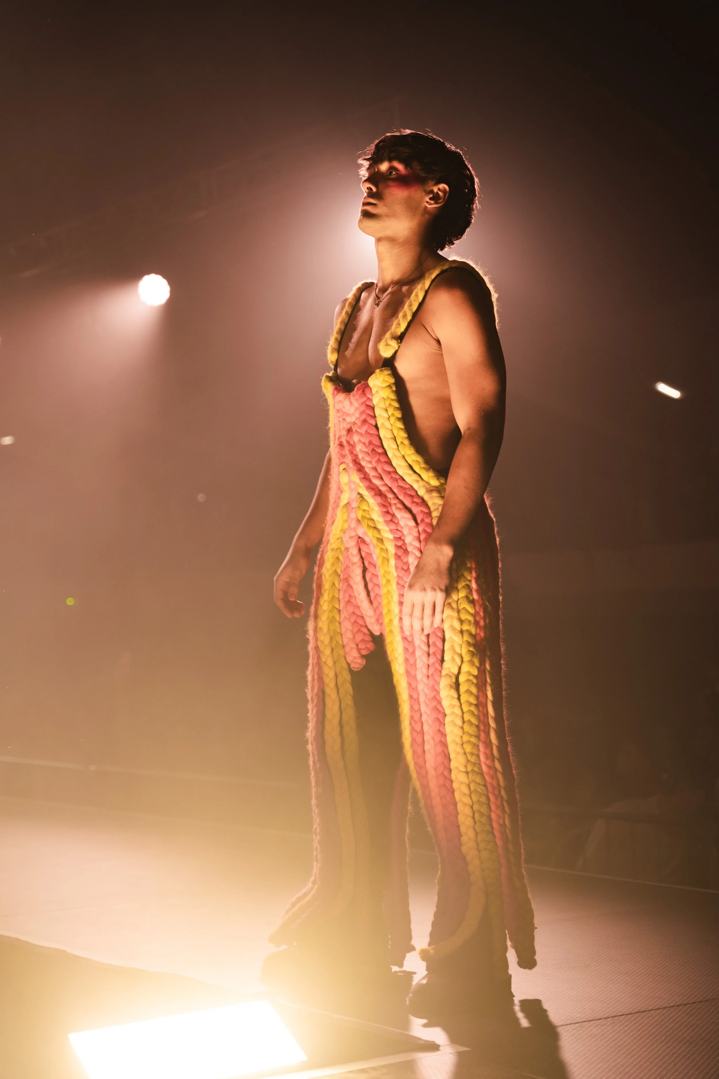 A person performing on stage wearing colorful, knitted pants and a matching top, illuminated by stage lighting.