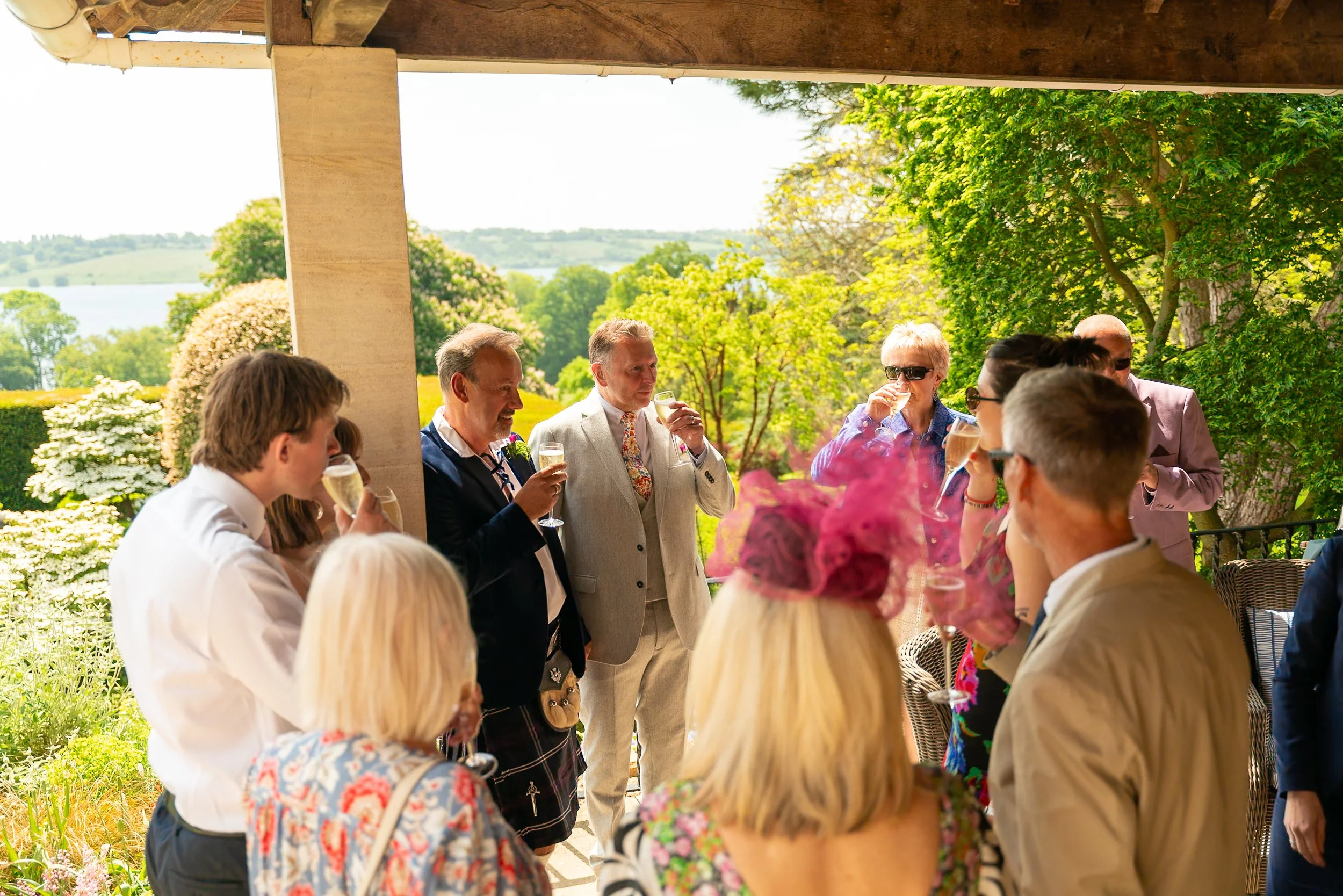 People gathered outdoors on a porch, celebrating with glasses of champagne on a sunny day surrounded by greenery.