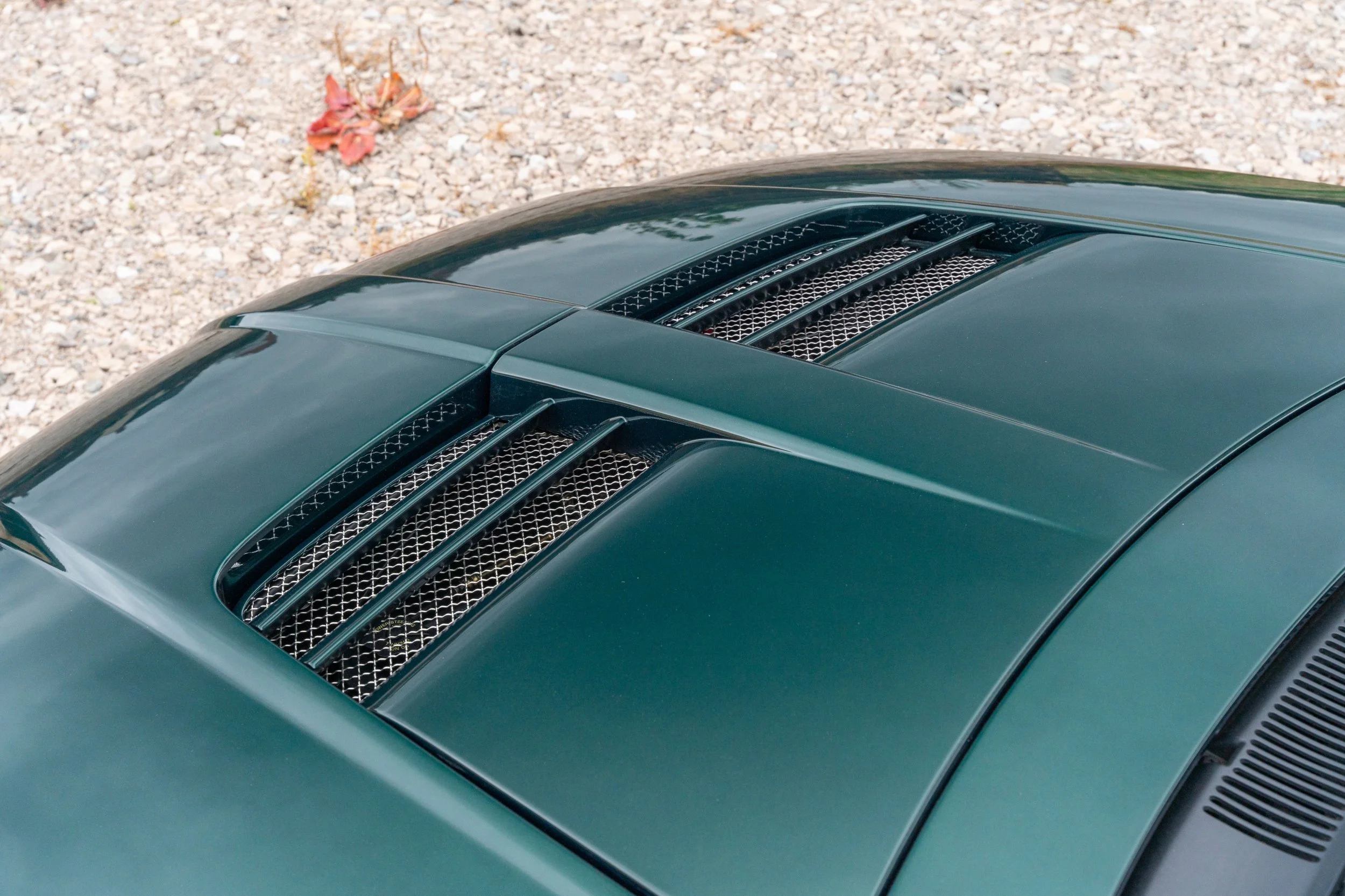 Close-up of the teal-green hood of a sports car with black vents and metal grilles.