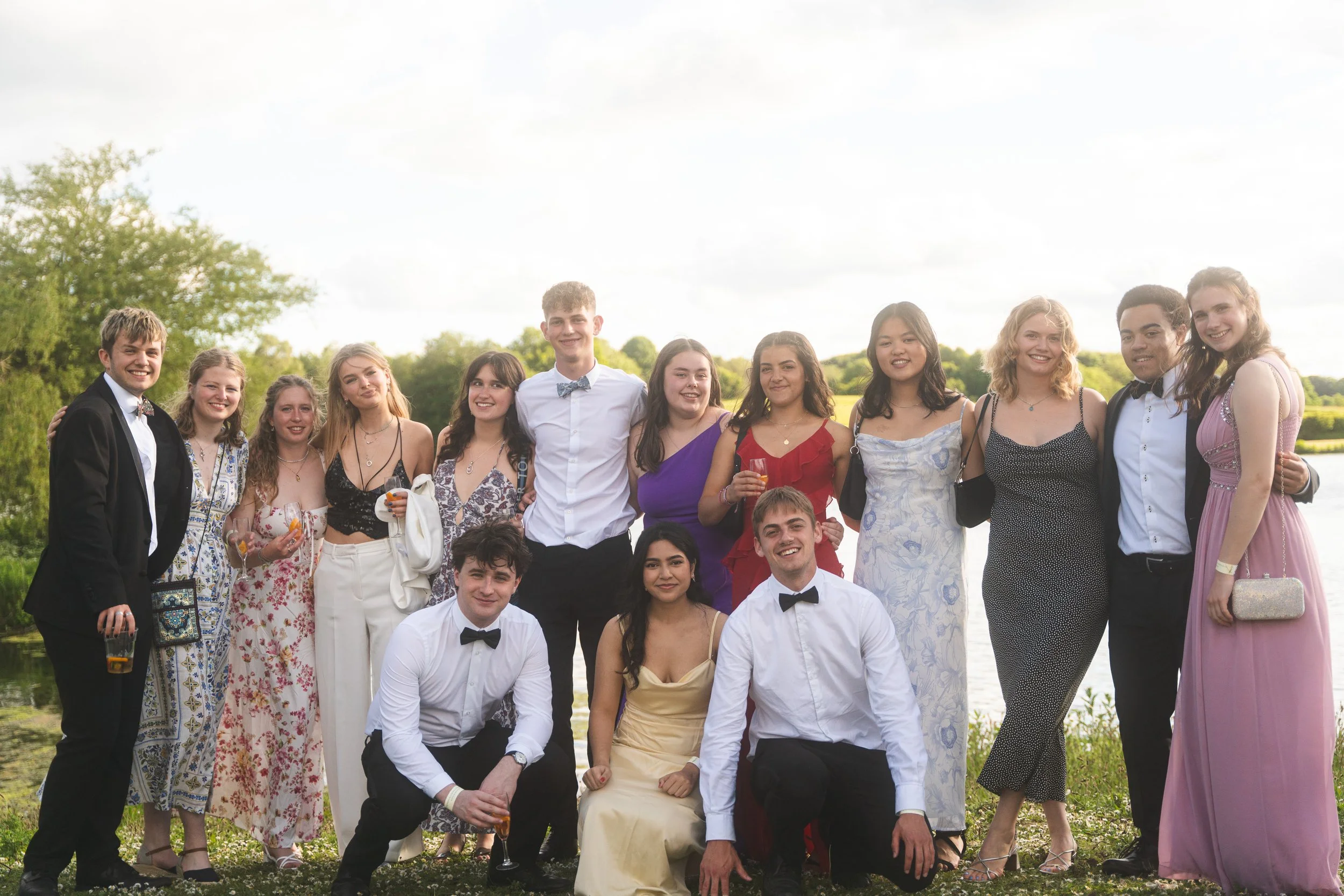 Group of young people dressed in formal attire posing outdoors near a body of water.