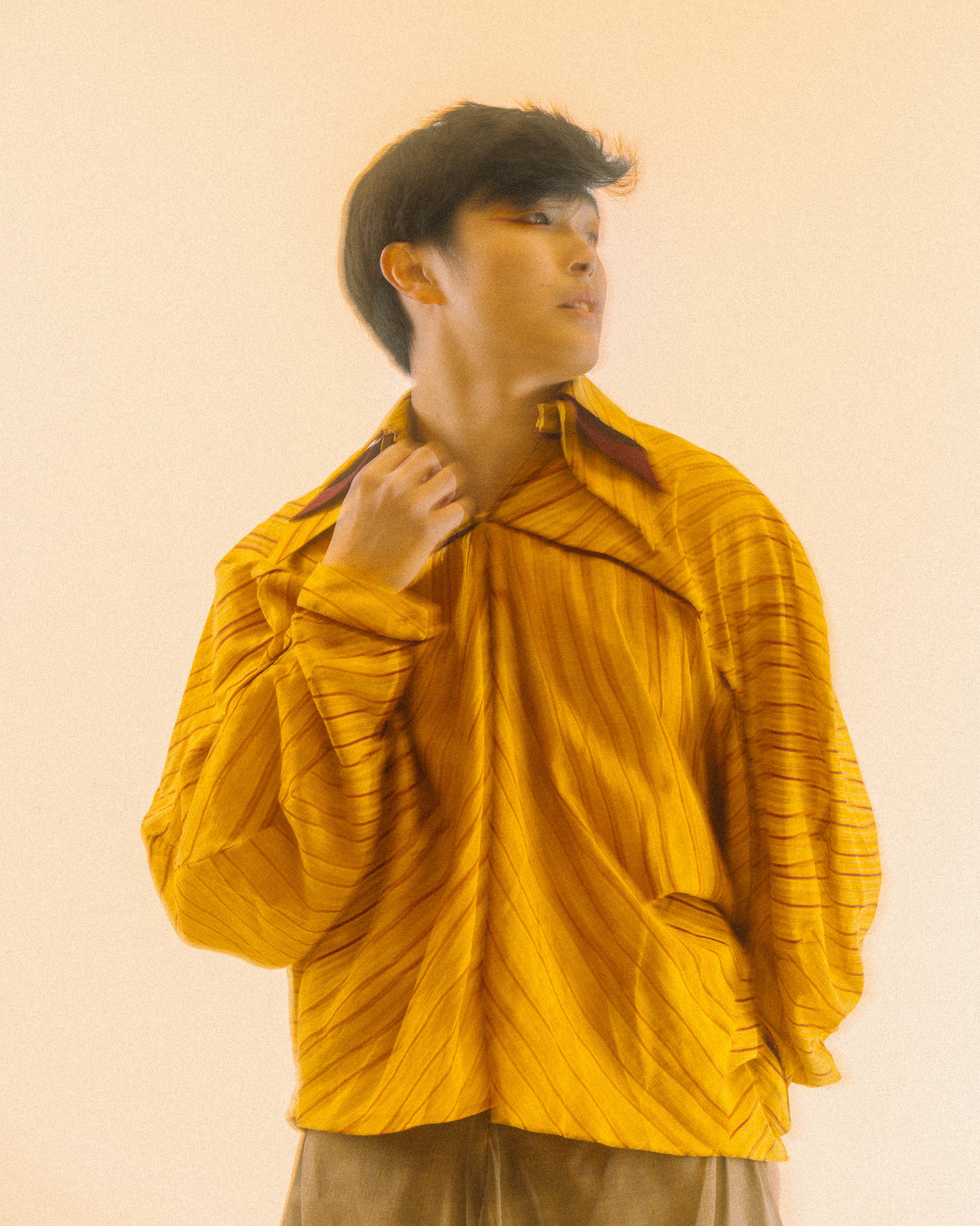 A person with dark hair wearing a loose yellow striped shirt with a collar, standing against a plain light-colored background.