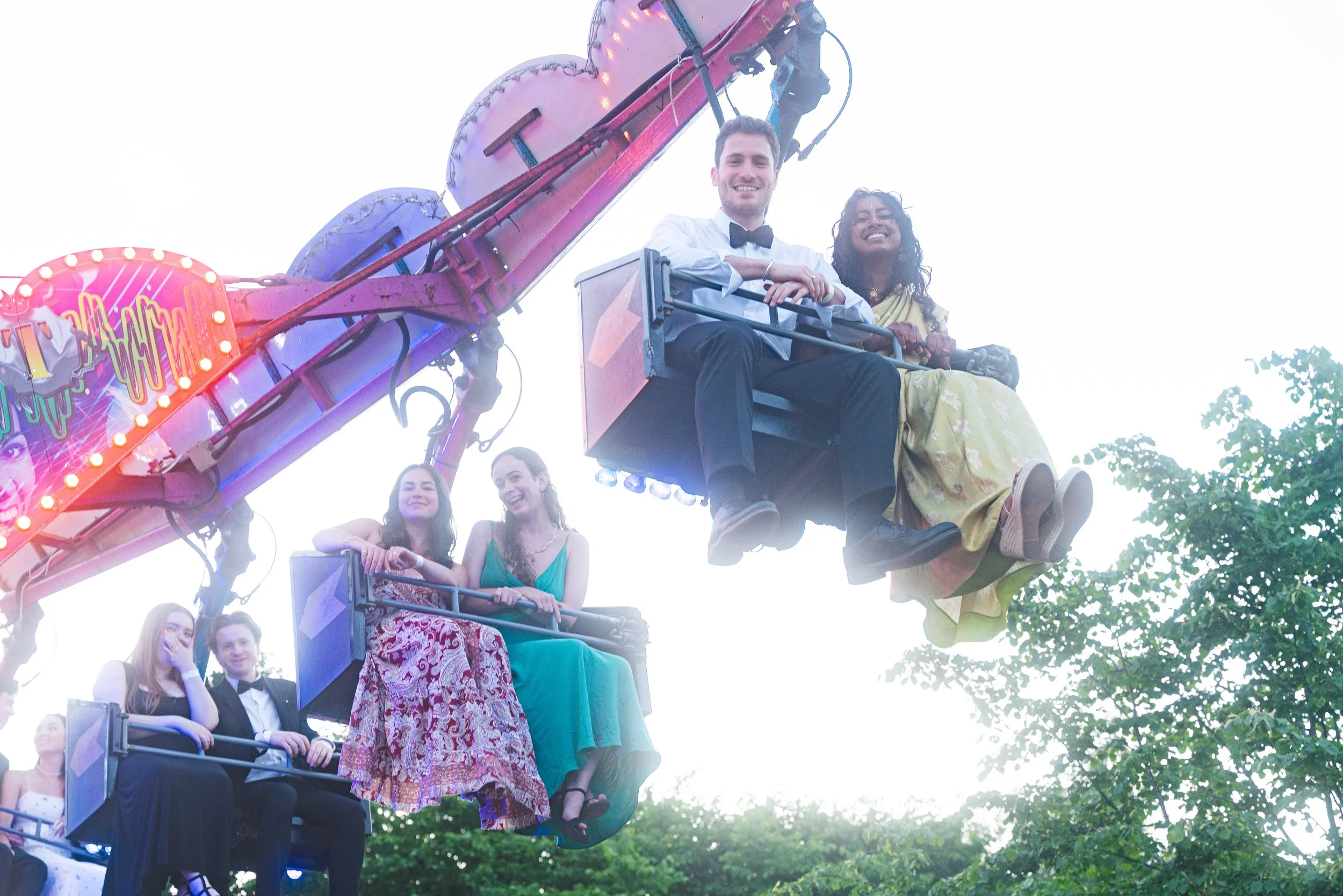 Group of people riding on a colorful amusement park swing ride with trees in the background.