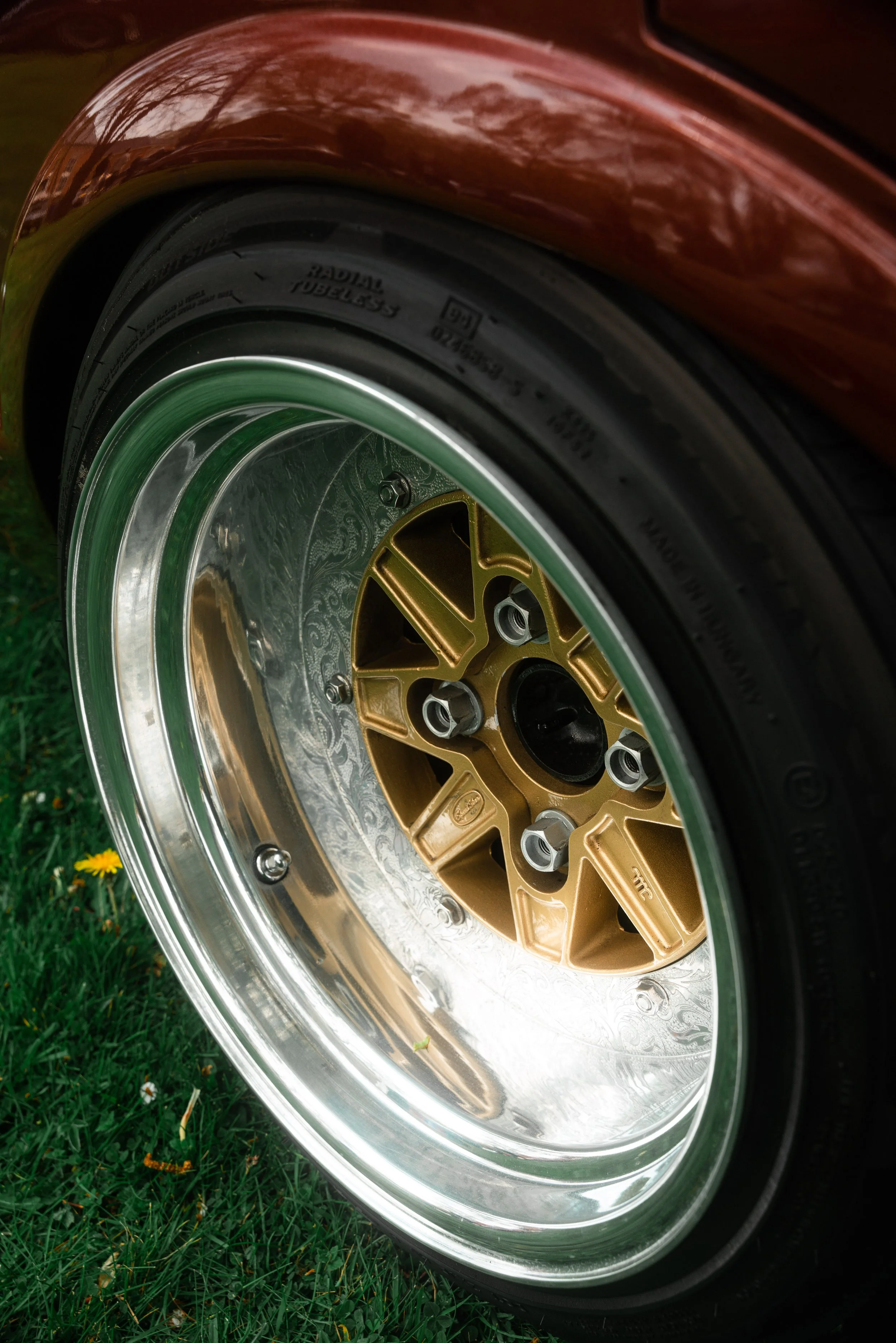 Close-up of a vintage car wheel with a gold-colored hubcap and chrome rim, on green grass.