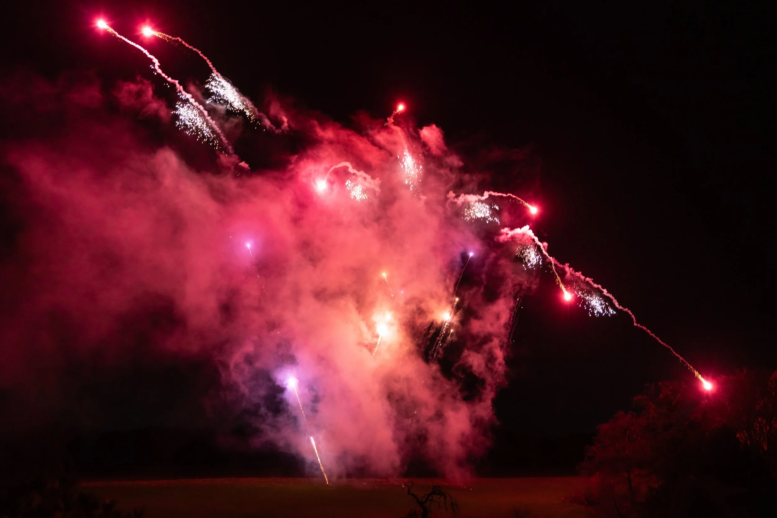 Fireworks display in the night sky with pink and red explosions and smoke.