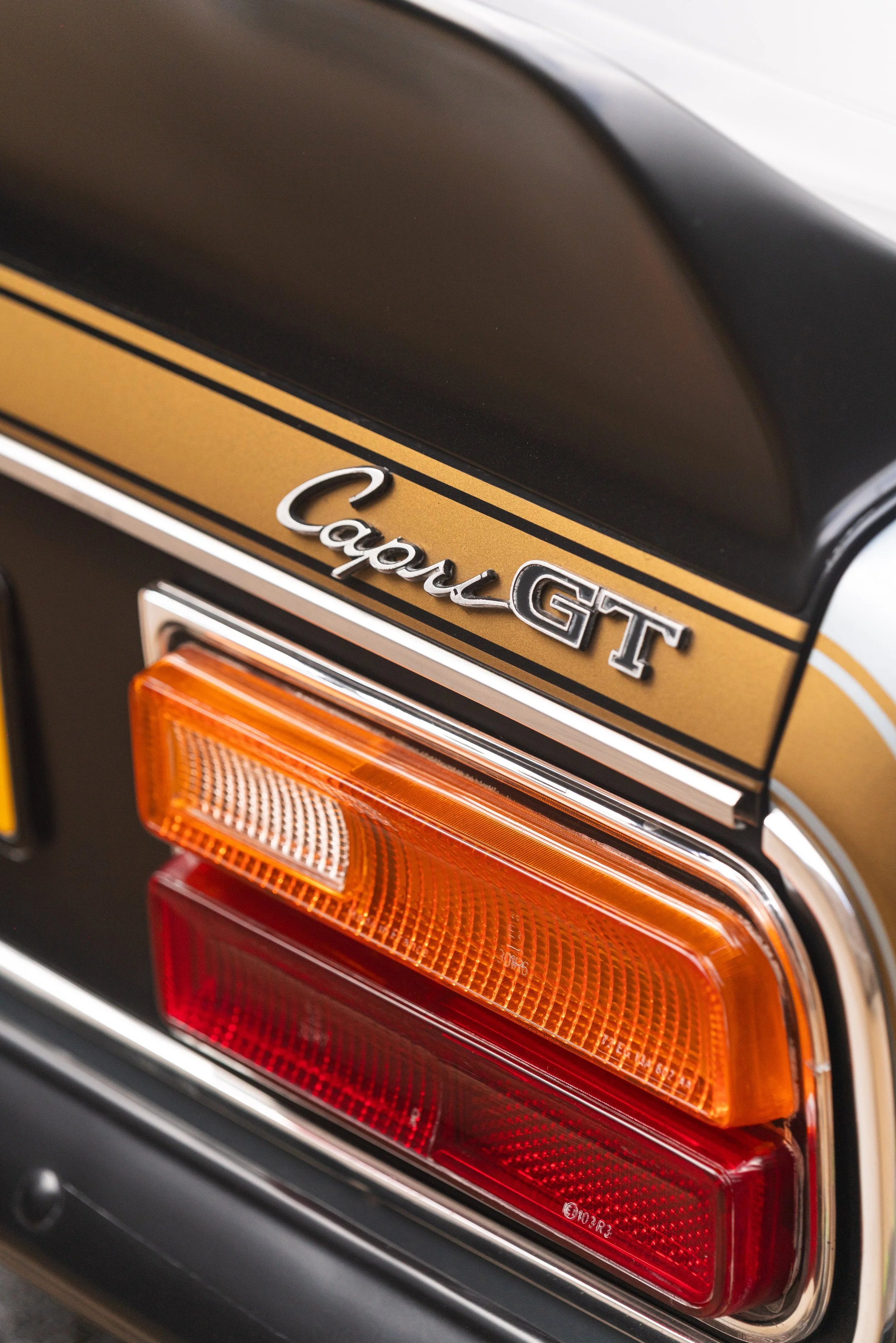 Close-up of a vintage car's rear end, showing the taillight and the badge that reads 'Capa G T' with a gold and black striped design.