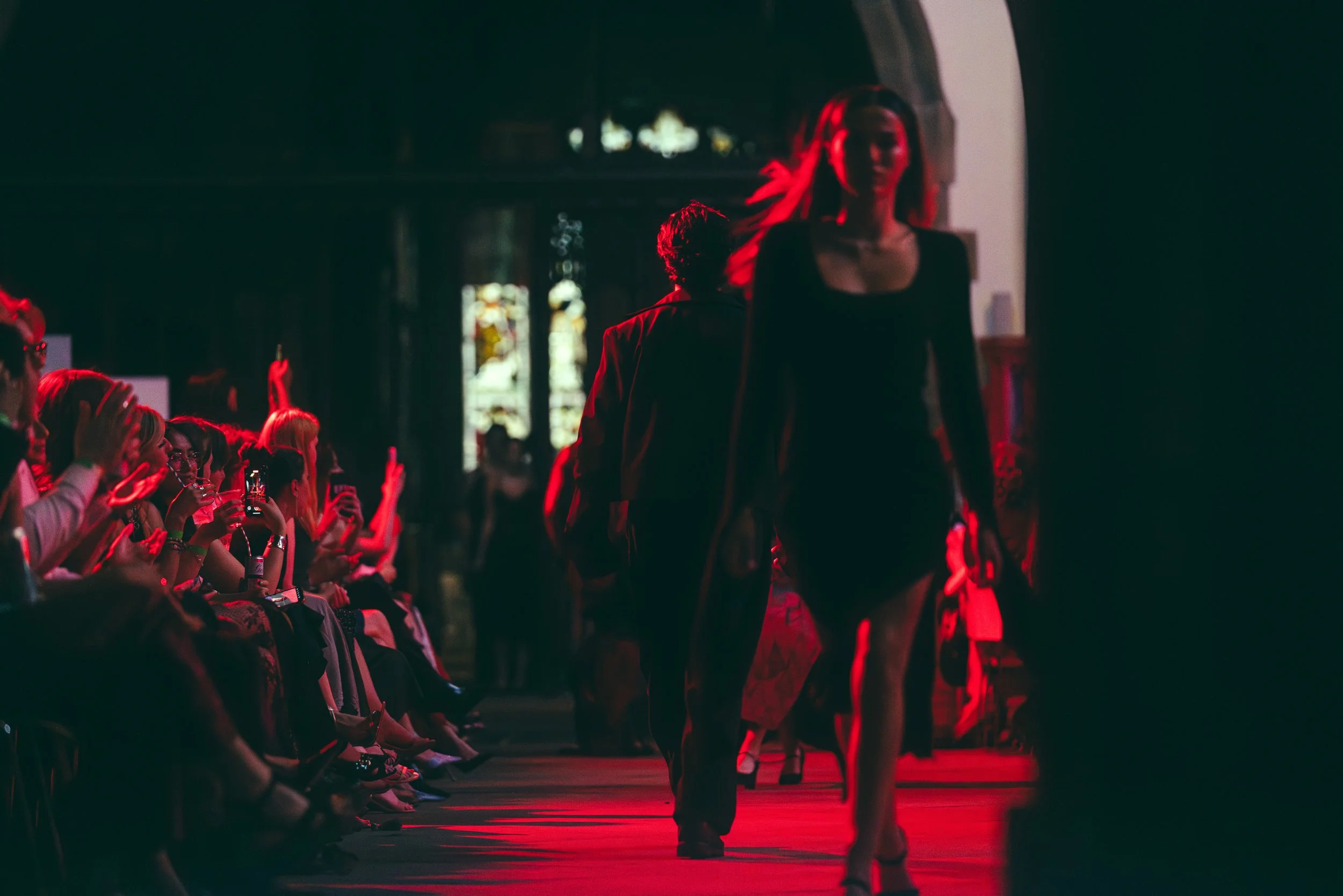 People attending a fashion show, with models walking down the runway and the audience taking pictures and watching.