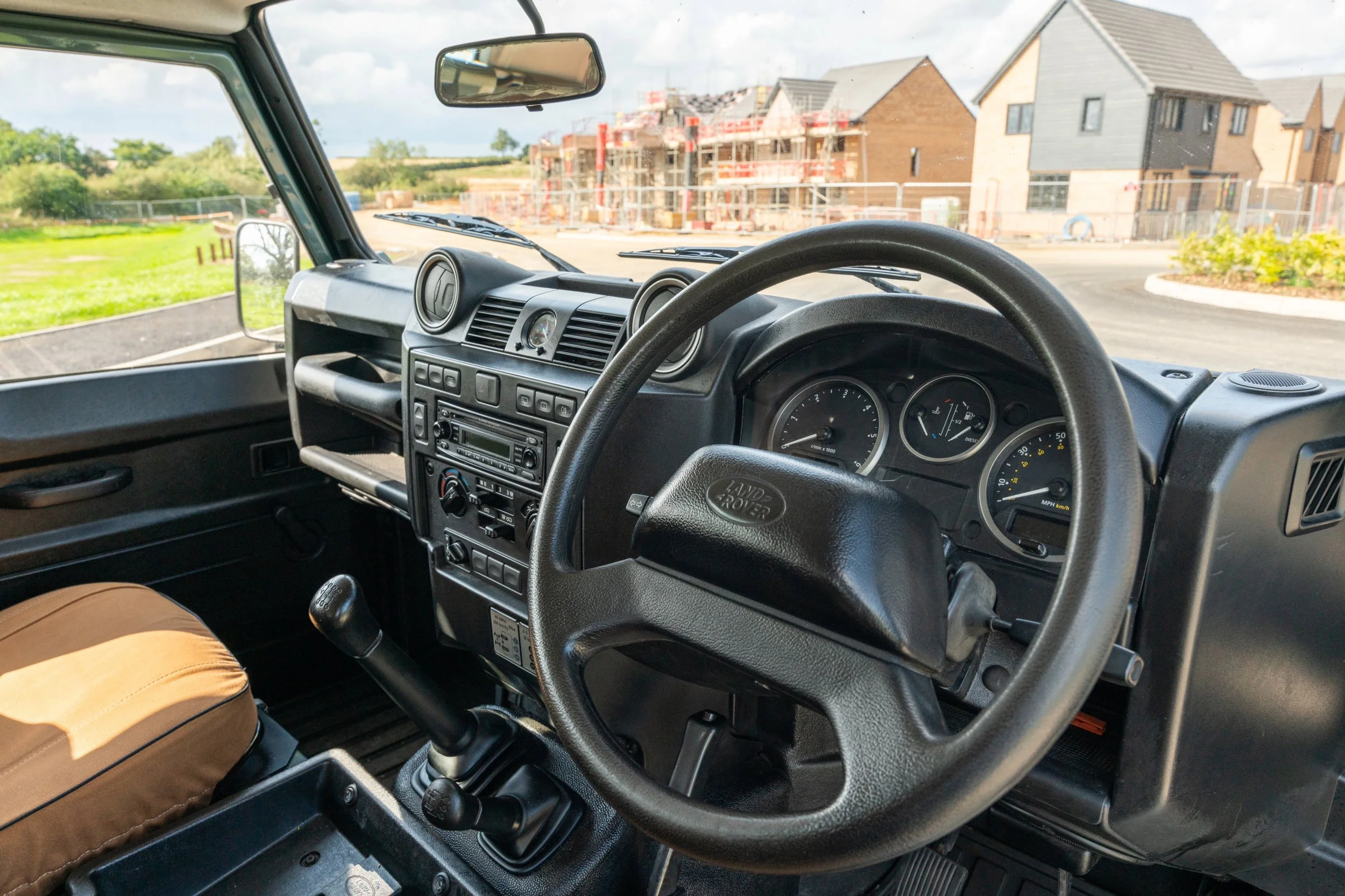 Interior view of a Land Rover vehicle with construction and houses visible through the windshield.
