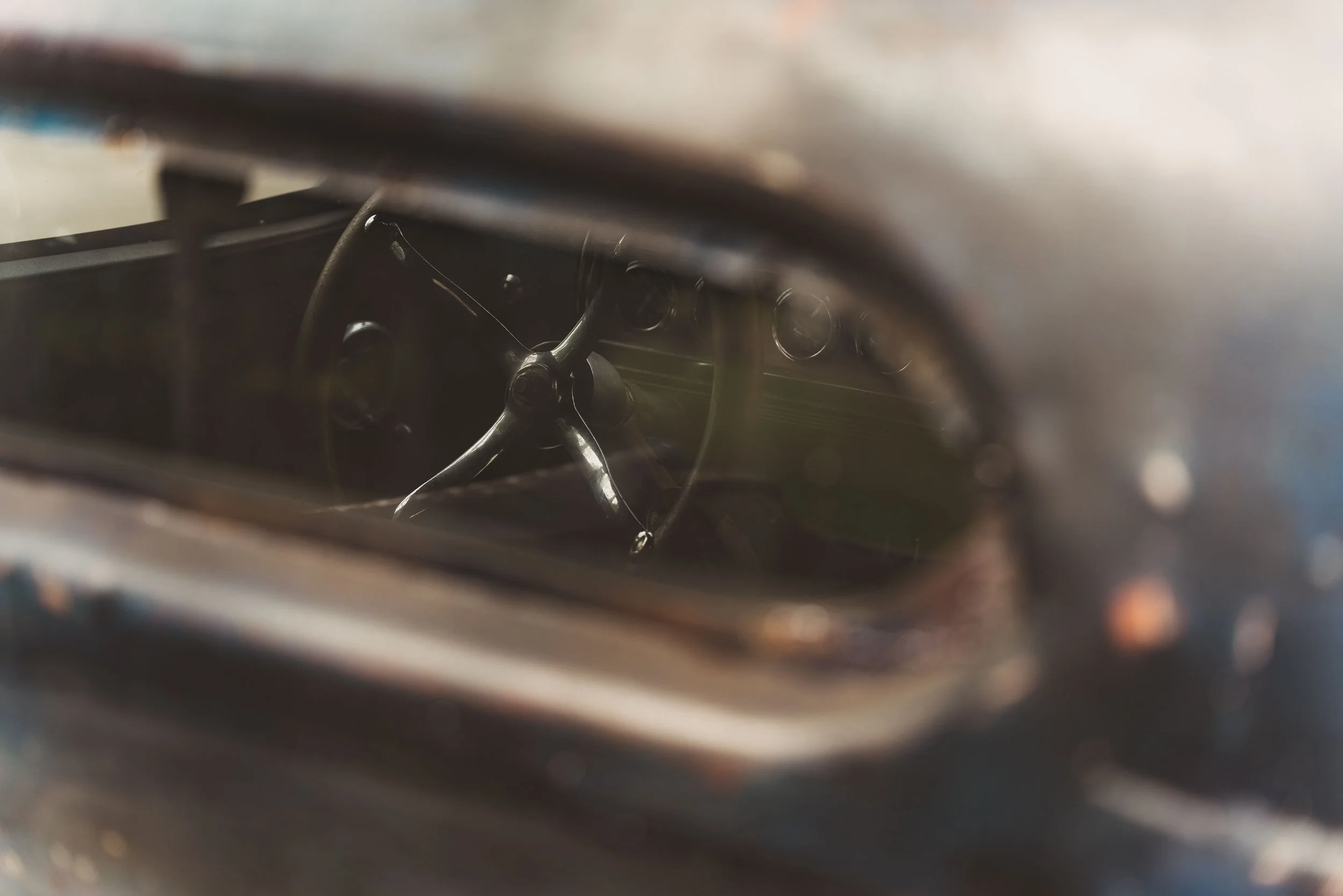 View of an old, vintage car's interior through the windshield, showing a black steering wheel and dashboard
