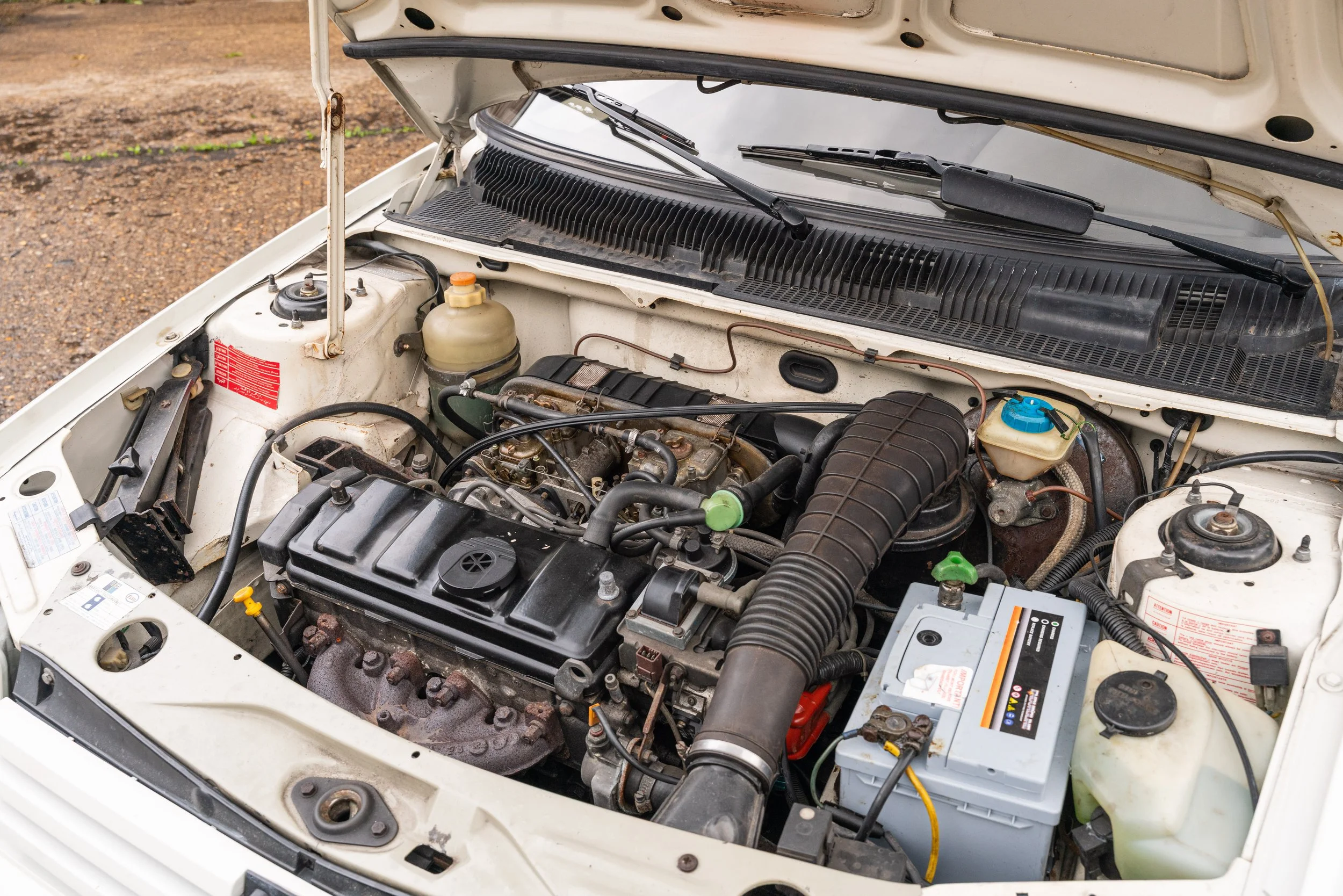 Open car hood showing engine and various engine components in a white vehicle.