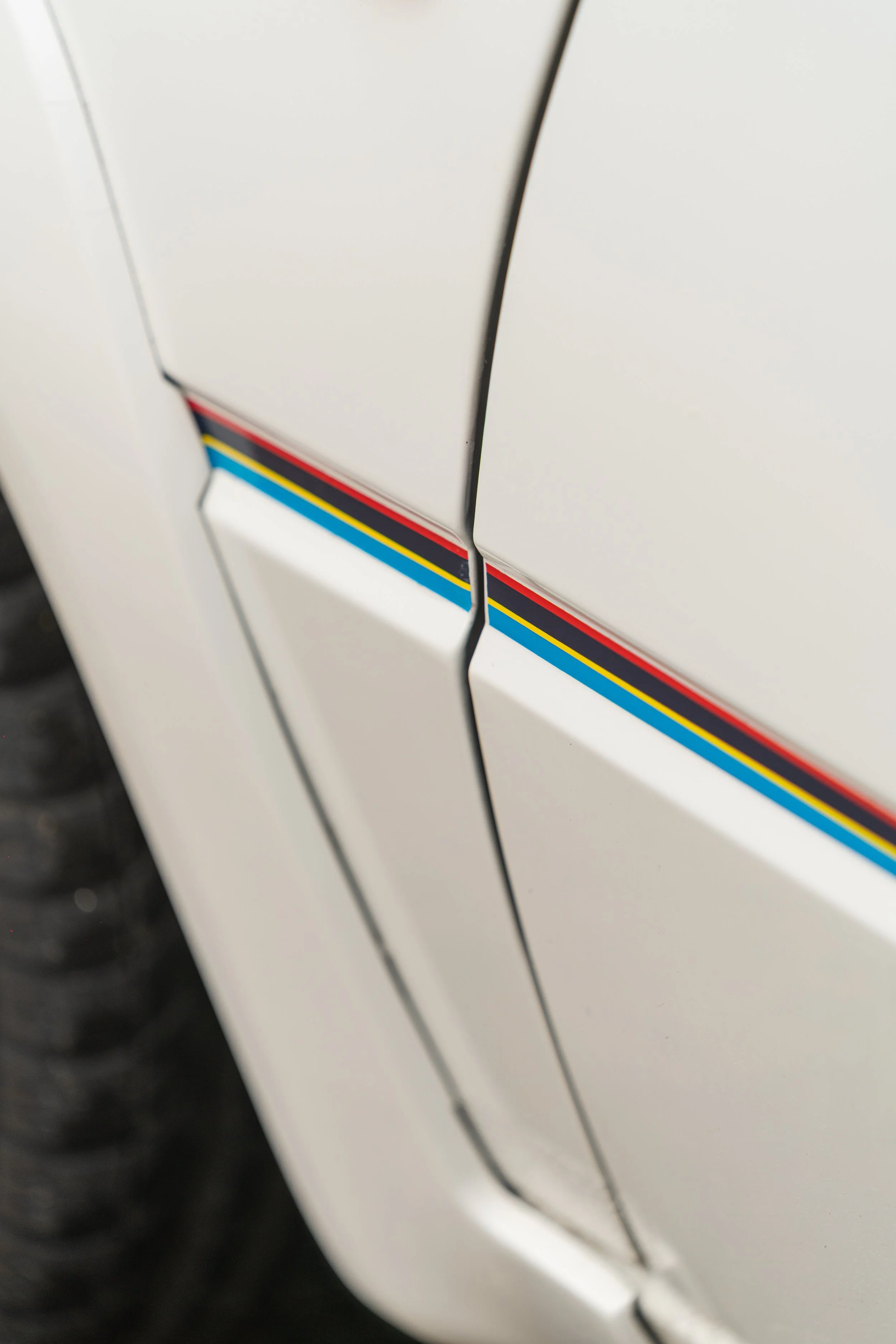Close-up of a white vehicle with racing stripes in red, blue, yellow, and black.