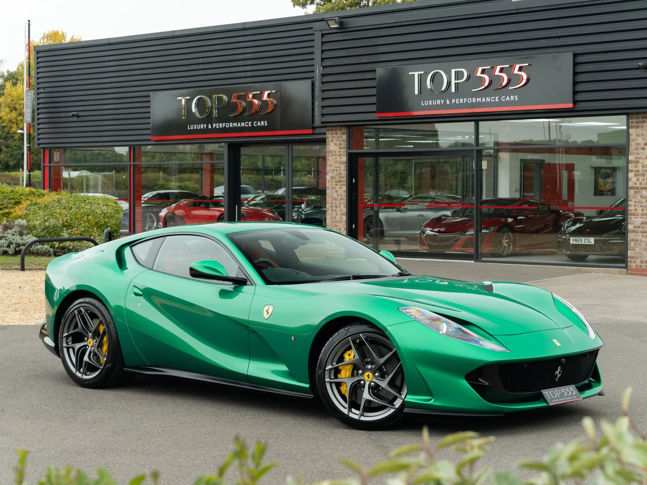 Green Ferrari sports car parked outside a luxury car dealership named Top 555.
